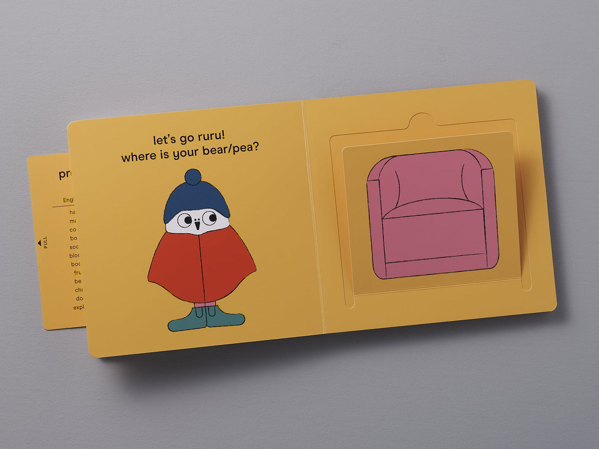 A children&#39;s board book opened to a page with a colorful illustration of a cartoon penguin and a flap revealing a pink armchair, accompanied by the text &quot;Let&#39;s Go Ruru&quot; – by Kate Muir.