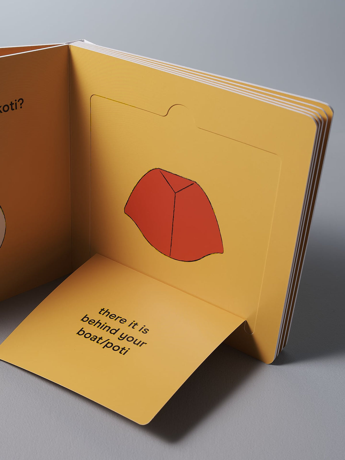 A Let&#39;s Go Ruru pop-up book by Kate Muir with a page displaying a red illustrated hat and text reading &quot;there it is behind your back!&quot; on an exciting adventure.