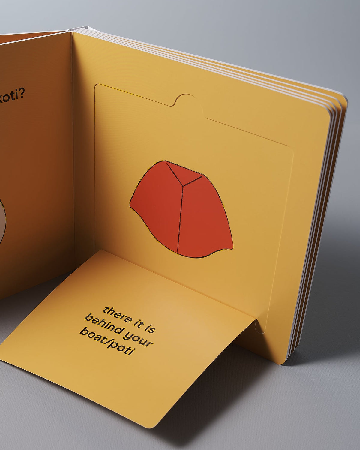 A Let's Go Ruru pop-up book by Kate Muir with a page displaying a red illustrated hat and text reading "there it is behind your back!" on an exciting adventure.