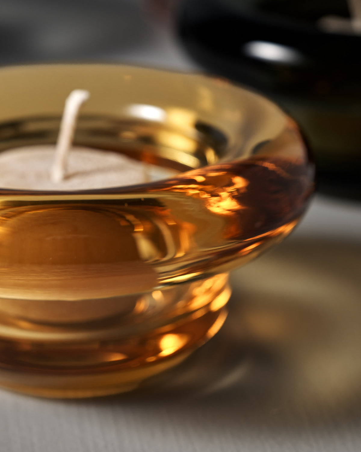 A close-up of a tea light candle in a Nedre Foss Sirkel Candle Holder – Amber Yellow, casting a subtle glow on a light surface.
