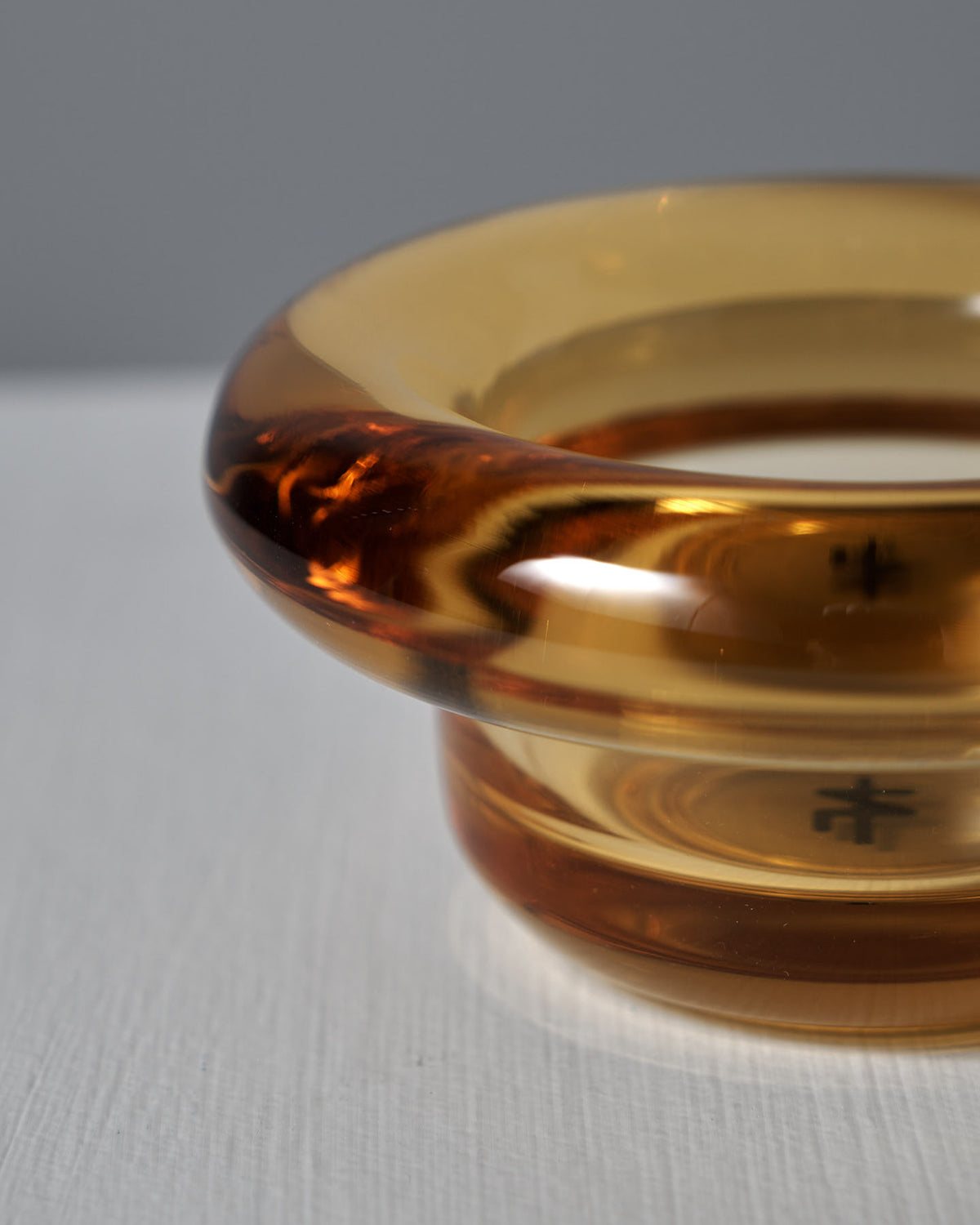 The Sirkel Candle Holder in Amber Yellow from Nedre Foss, evoking a pressed glass look, is elegantly displayed on a white surface as a tea-light holder.