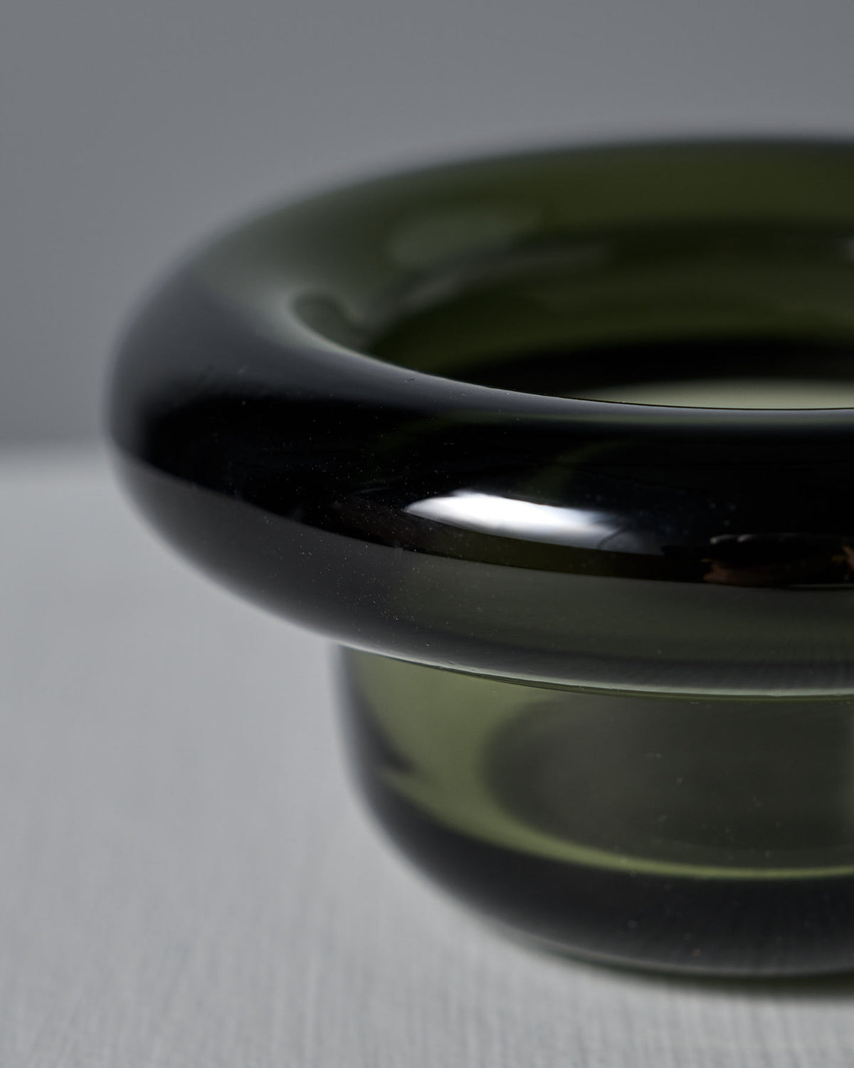Close-up of a glossy, dark green pressed glass object with a rounded, hollow doughnut-like shape. The Forest Green Sirkel Candle Holder by Nedre Foss elegantly sits on a light surface, reminiscent of a sophisticated tea-light holder.