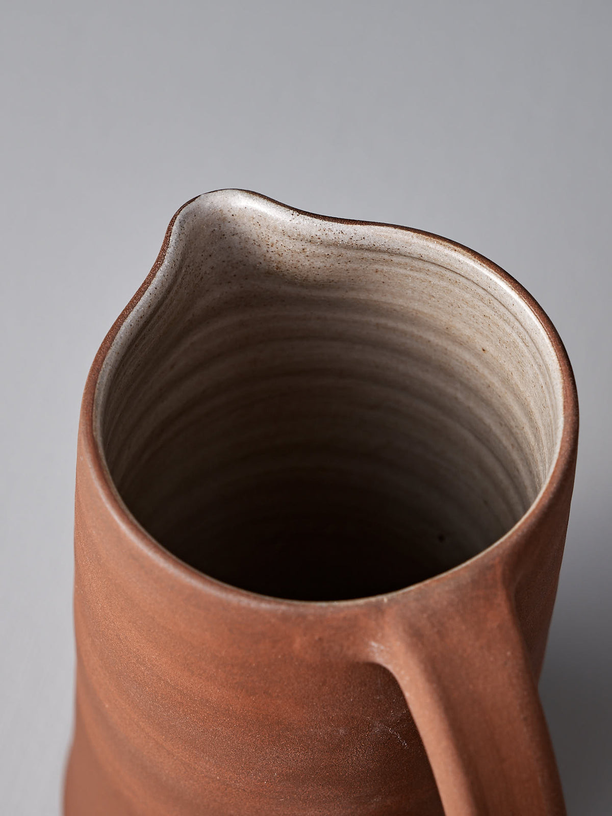 Top view of a handmade Jug – Brick Red by Nicola Shuttleworth with a spout and handle. The exterior boasts a rich, brown satin glaze, while the interior is a lighter color with visible pottery lines.