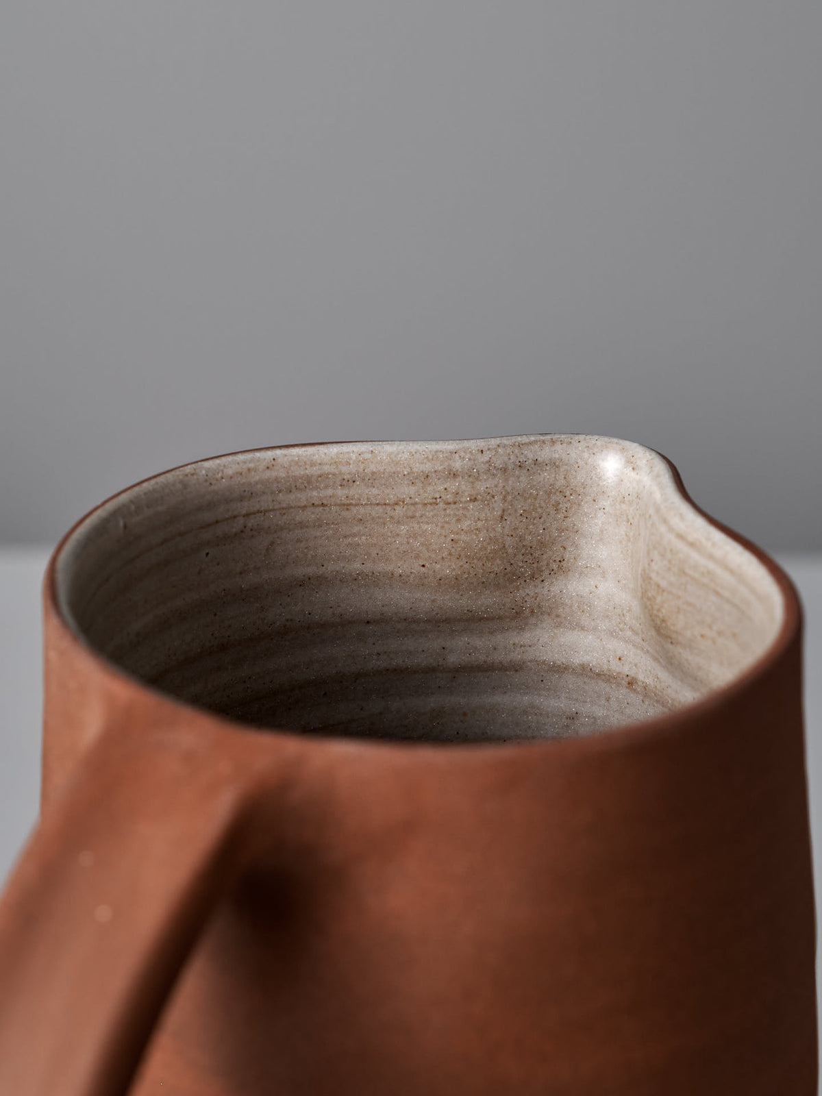 Close-up of the rim and handle of a Jug – Brick Red by Nicola Shuttleworth, showcasing its textured, brown ceramic surface with a light interior and satin glaze finish.