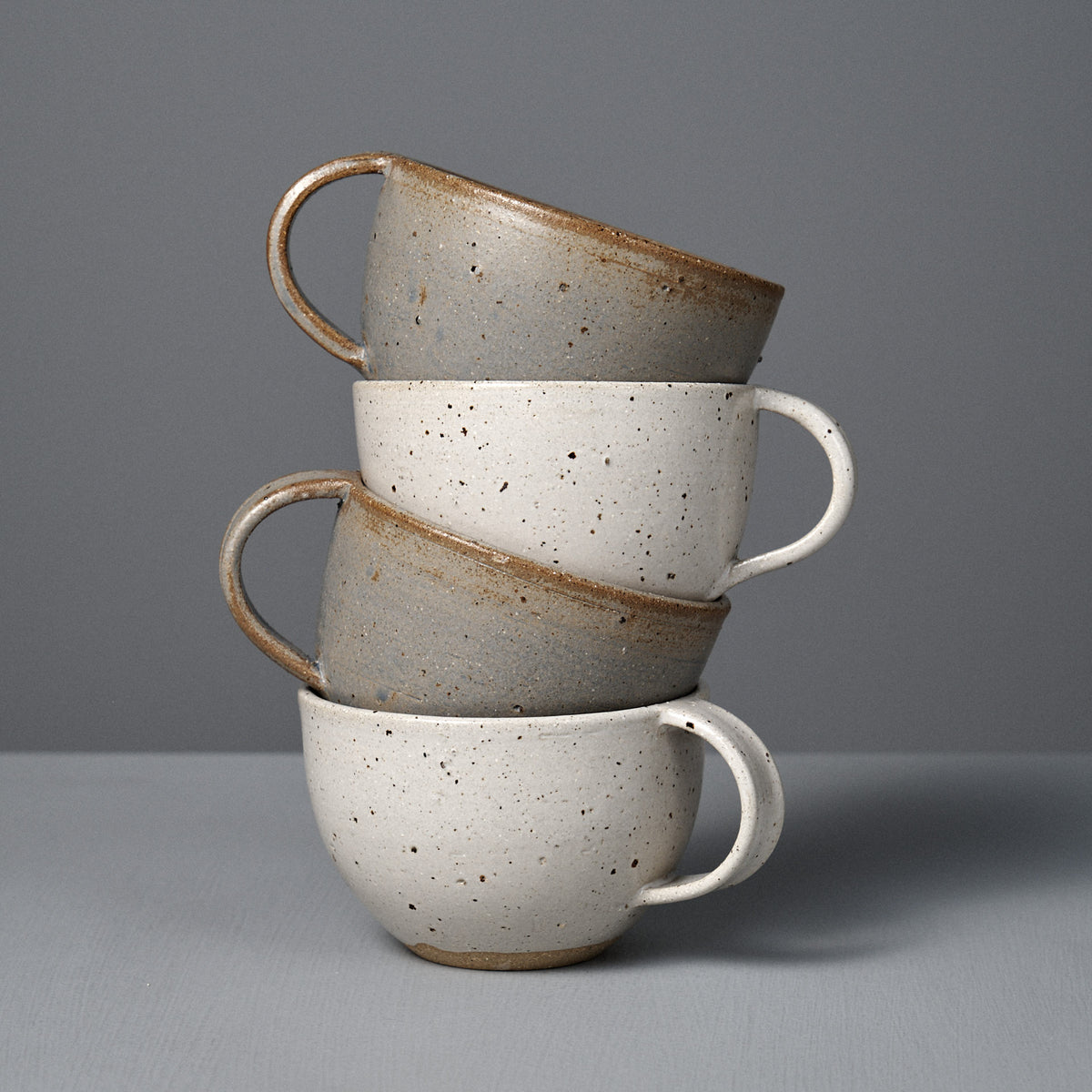 Three Cup – Speckled White pieces, each handmade with a satin speckled glaze, are stacked on their sides against a gray background.