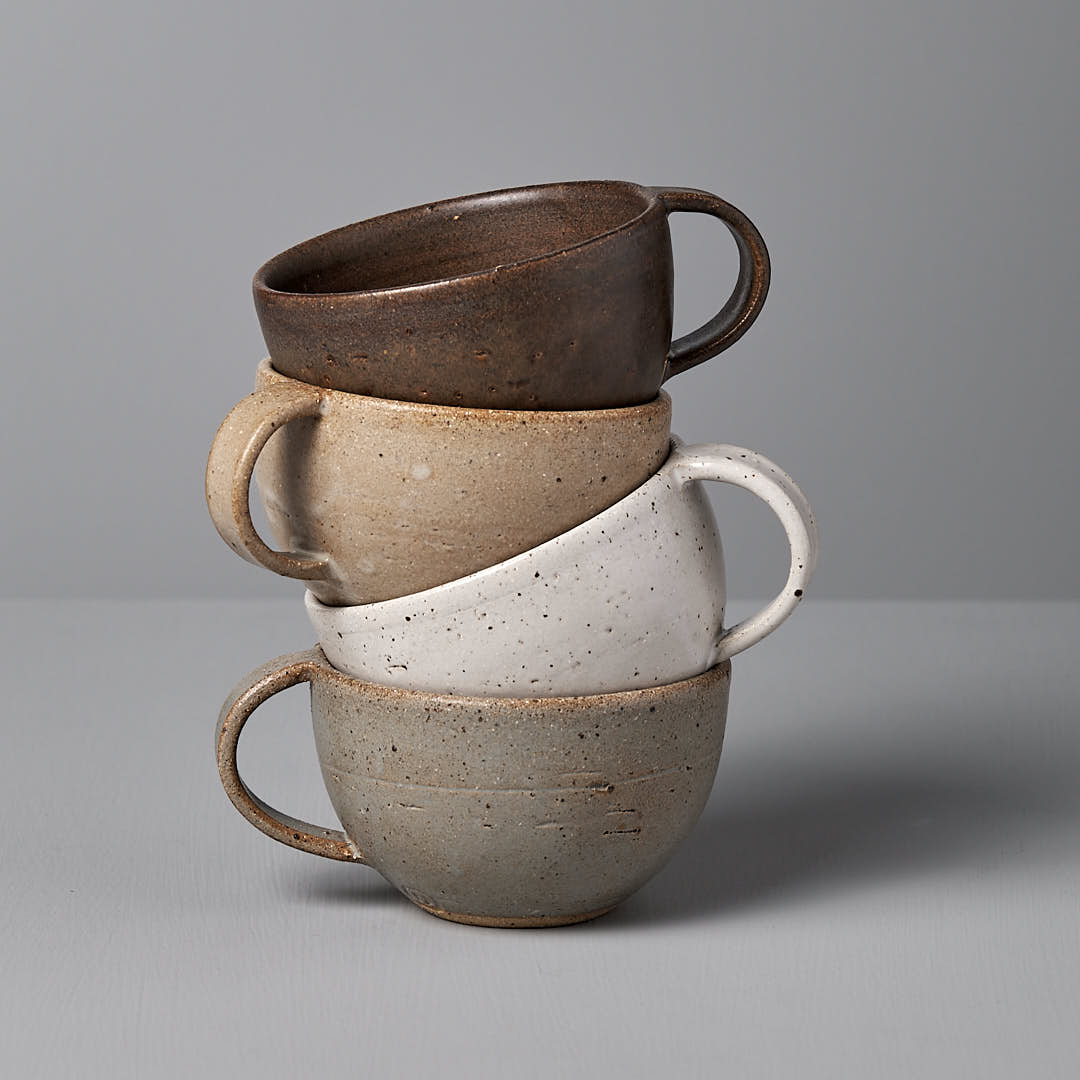 A stack of four ceramic cups in different earthy tones against a plain grey background.