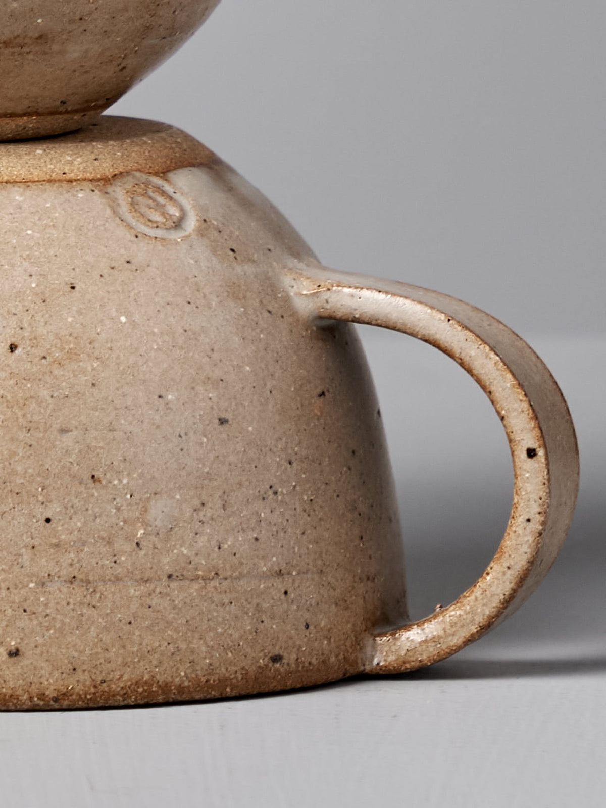 Close-up of the handle of the Cup – Light Brown by Nicola Shuttleworth, showcasing a beige speckled texture with subtle variations in color. This handmade cup features a wide rimmed design and is expertly finished with a blue ash satin glaze.