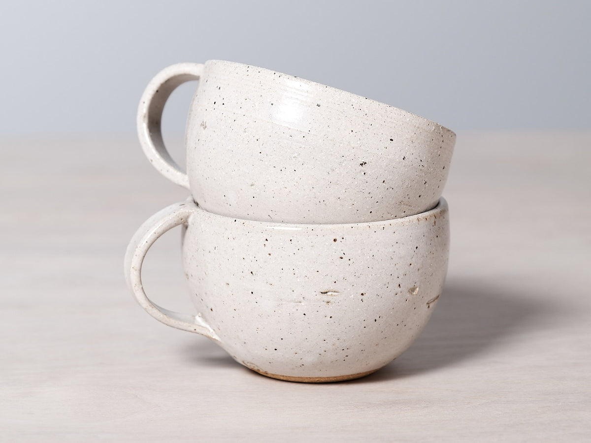 Two handmade Nicola Shuttleworth speckled cups stacked on top of each other, with a glossy glaze finish.