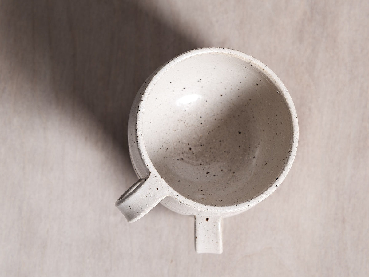 A handmade Speckled cup, inspired by Wellington, sitting on top of a wooden surface.
