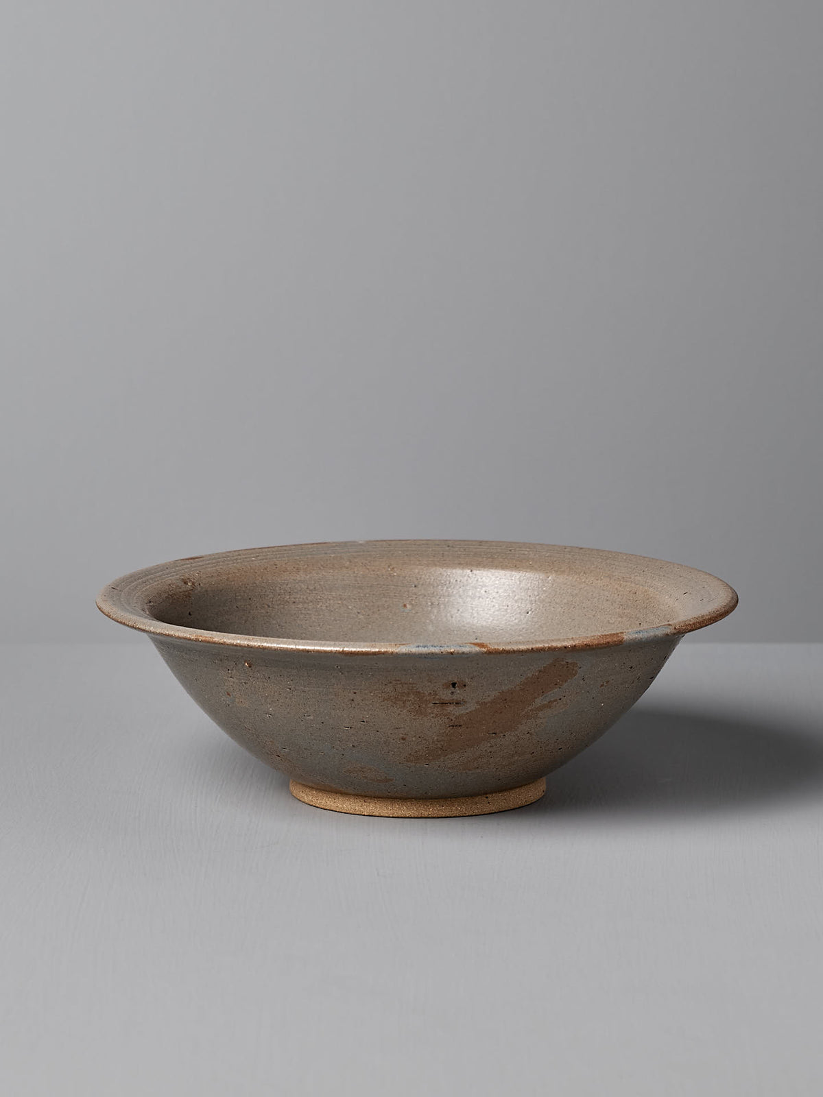 A shallow gray ceramic serving bowl, featuring a wide rim and handmade stoneware design by Nicola Shuttleworth, sits on a flat surface against a plain gray background. This exquisite piece is named &quot;Serving Bowl – Blue Ash&quot; and hails from Pōneke Wellington.