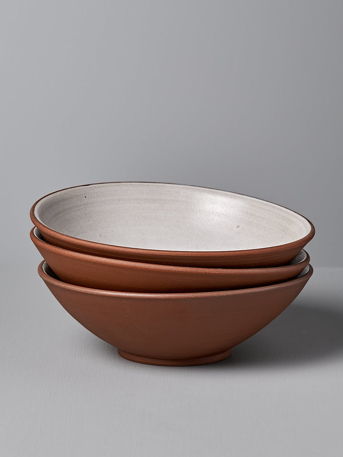 Three Nicola Shuttleworth Serving Bowls – Red Clay, stacked with a brown exterior and white interior, placed against a gray background.