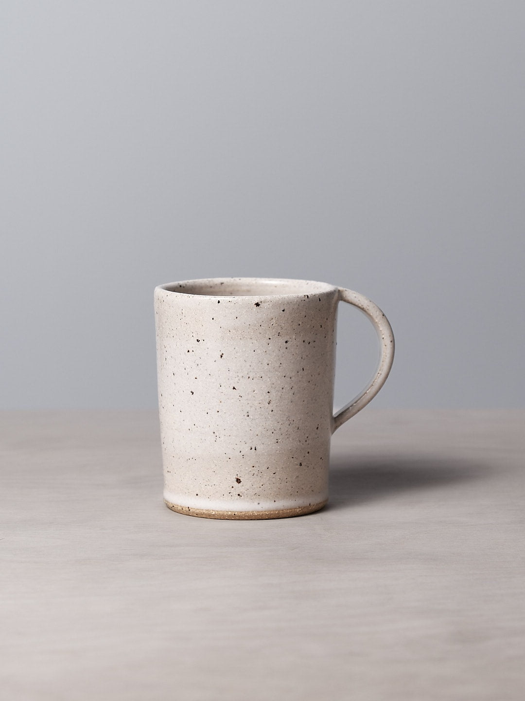 A handmade Speckled mug with a satin glaze sitting on a table with a grey background, made by Nicola Shuttleworth.