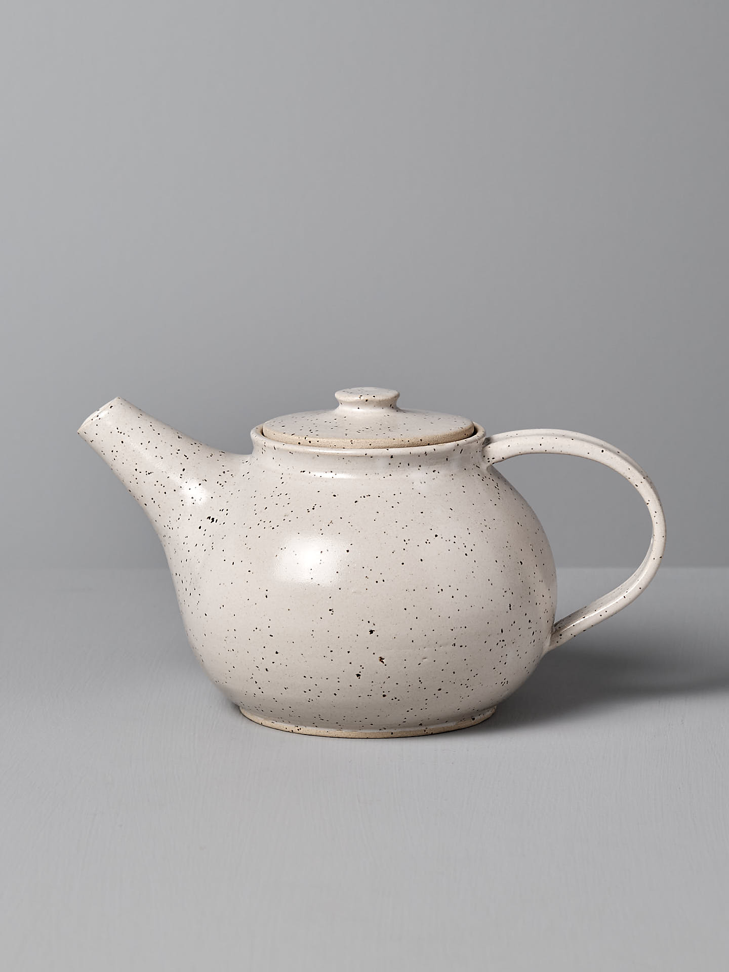 A Nicola Shuttleworth "Tea Pot – Speckled," featuring a handmade design with a rounded body, short spout, and curved handle, sits gracefully against a gray background, evoking the charm of Wellington craftsmanship.