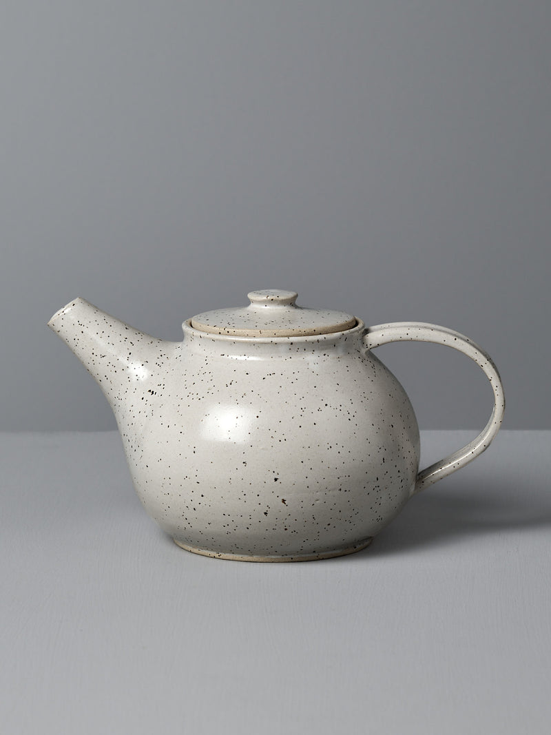 A Nicola Shuttleworth "Tea Pot – Speckled," featuring a handmade design with a rounded body, short spout, and curved handle, sits gracefully against a gray background, evoking the charm of Wellington craftsmanship.