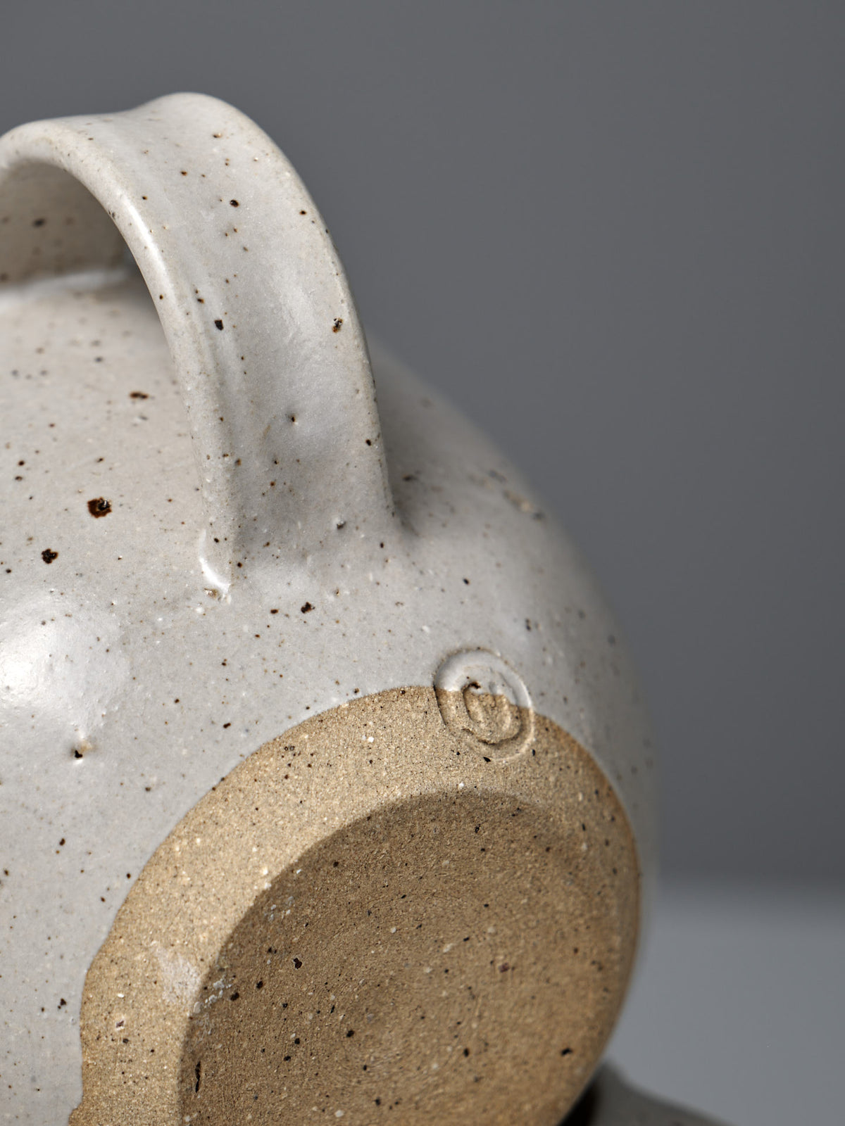 Close-up of the Cup – Speckled White, featuring a handmade design with a speckled satin glaze, unglazed circular base, and embossed maker&#39;s mark.