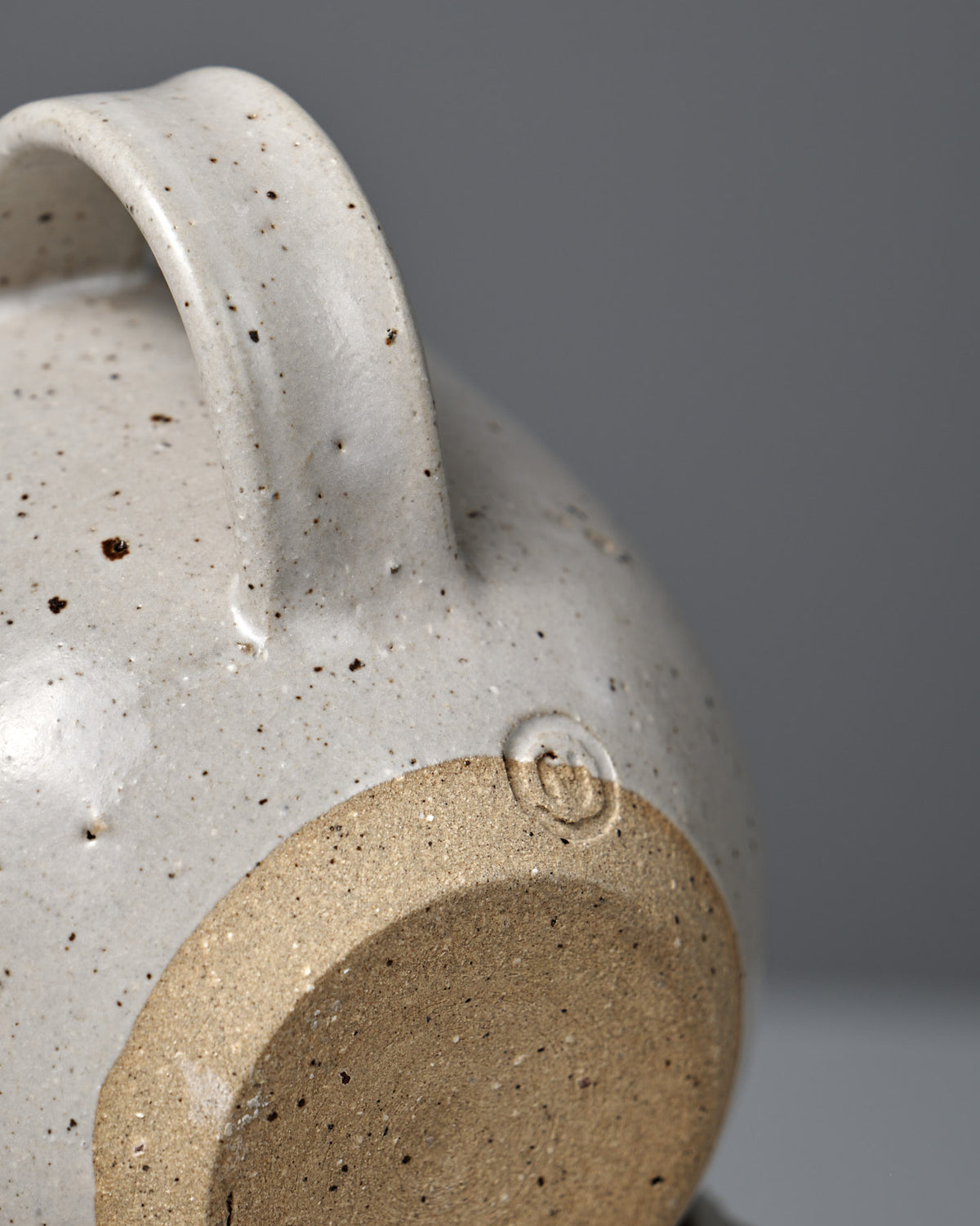 Close-up of the Cup – Speckled White, featuring a handmade design with a speckled satin glaze, unglazed circular base, and embossed maker's mark.