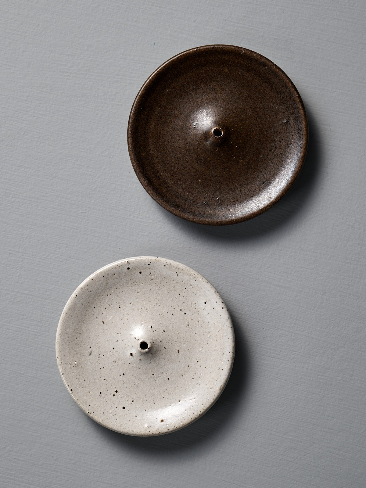 Two ceramic incense holders, one brown and one speckled white, on a gray background