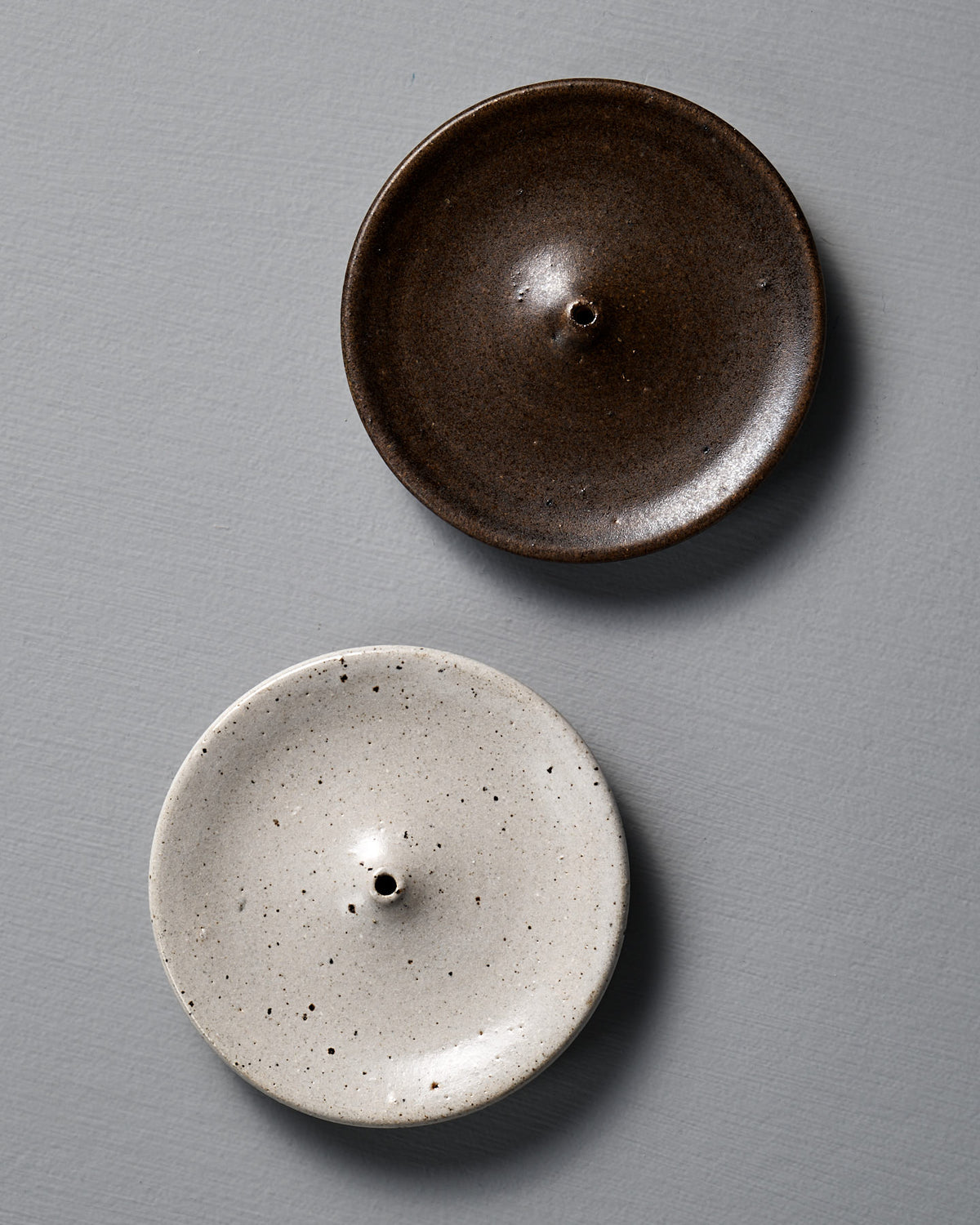 Two ceramic incense holders, one brown and one speckled white, on a gray background