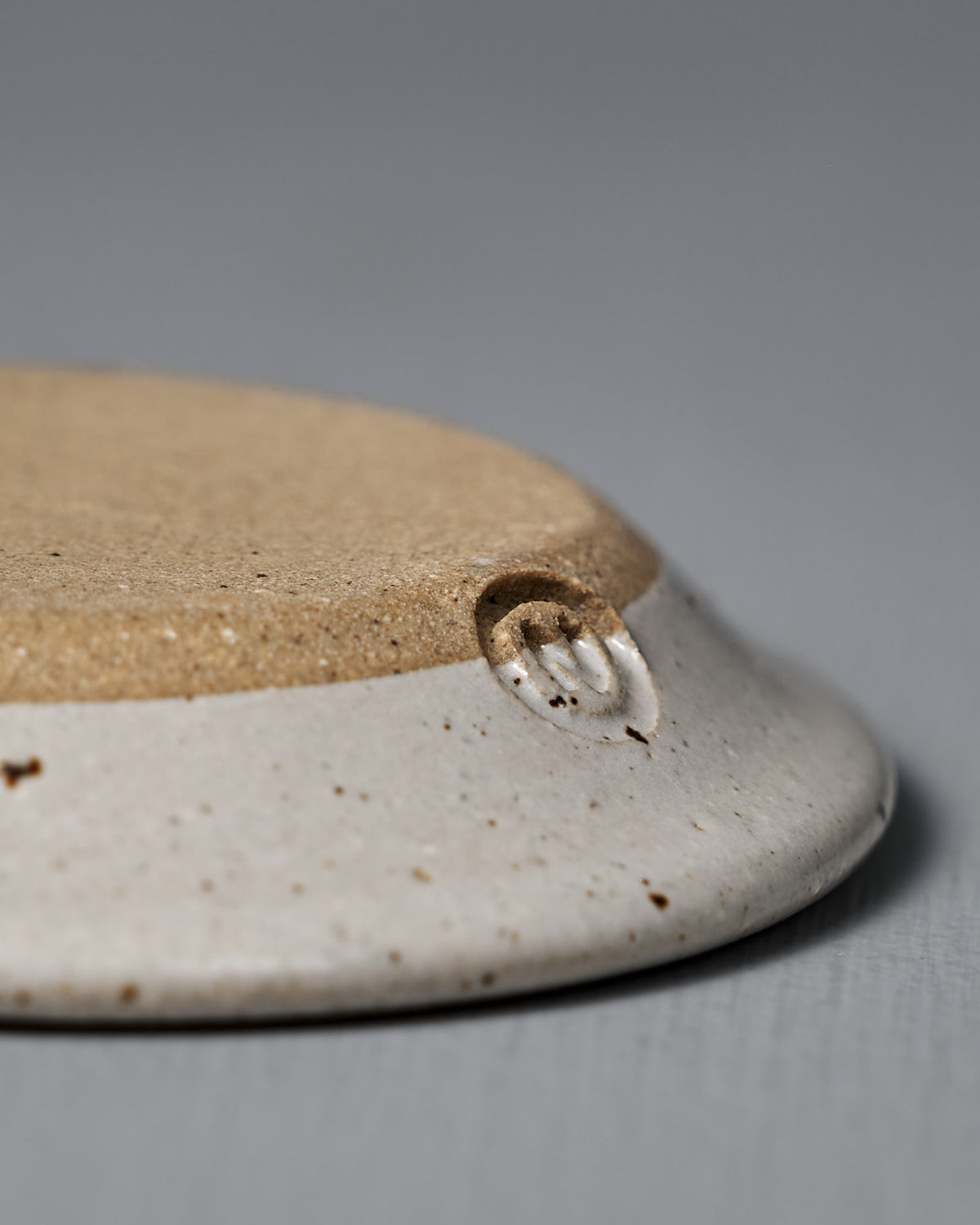 A close-up of the Incense Holder – Speckled White, a handmade stoneware piece with a matte beige center, white glazed rim, and a small maker’s mark near the edge, crafted in Wellington.