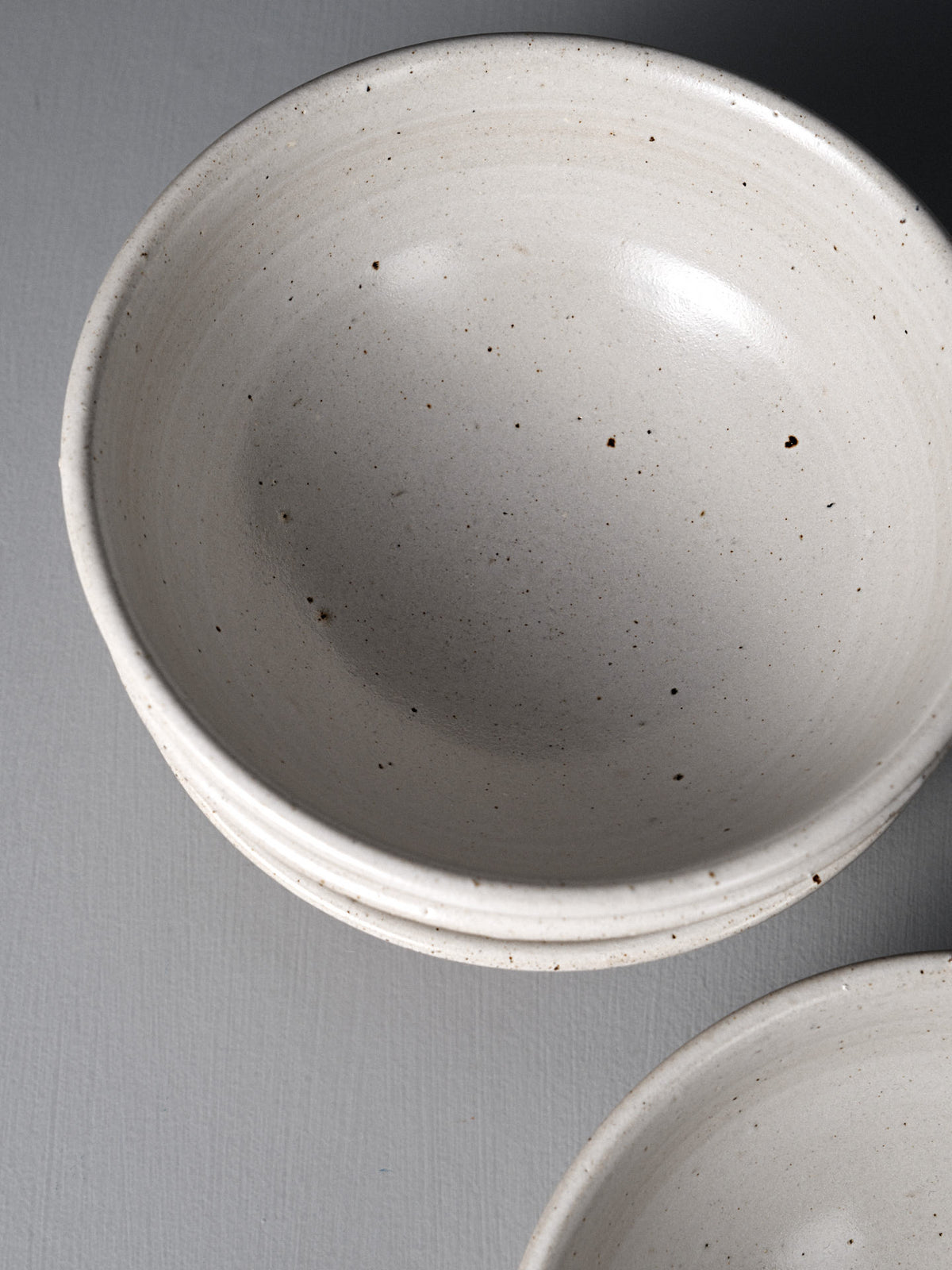 Three stacked Ridge Line Bowls with a speckled white glaze and matte finish rest on a gray surface, photographed from above—a beautiful example of Wellington pottery craftsmanship.