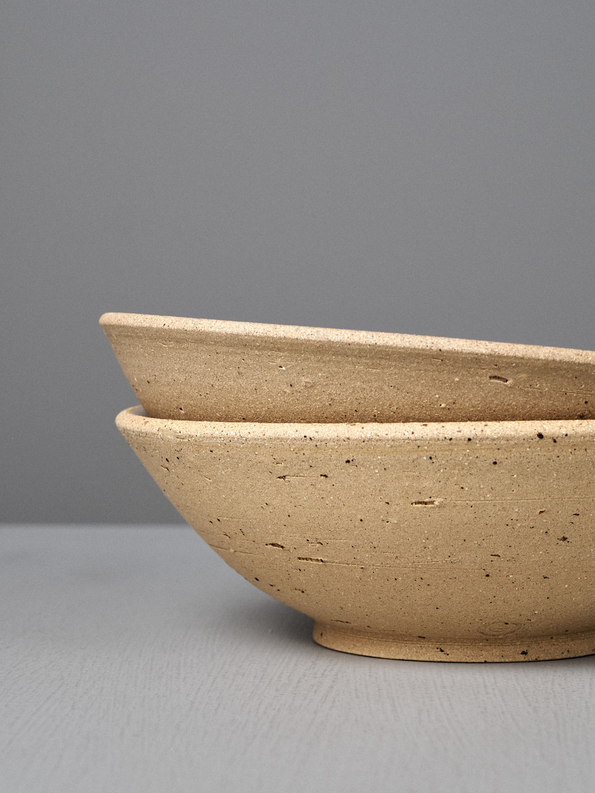 The Speckled Toast Serving Bowl – Large, a handcrafted beige bowl with a speckled finish made in Wellington, is displayed stacked on a gray surface against a plain gray background, highlighting the charm of handmade ceramics.