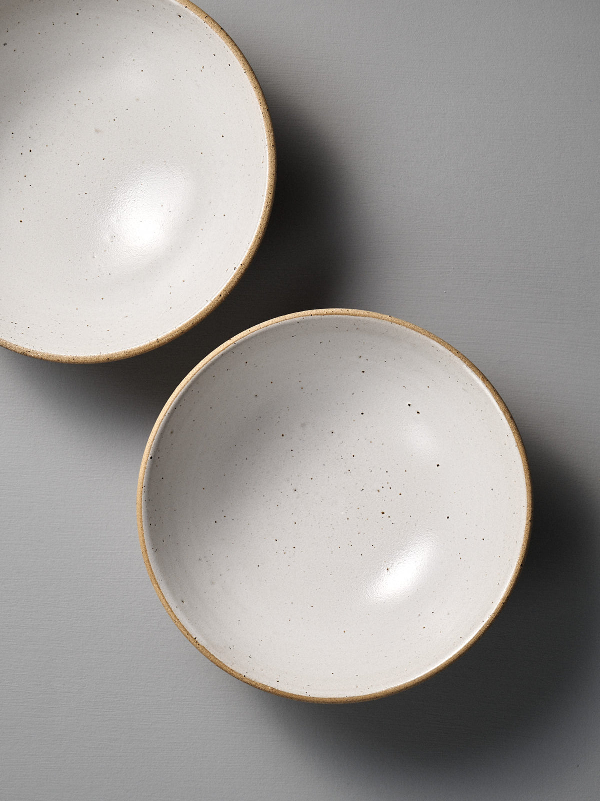 The Speckled Toast Serving Bowl – Large is a round, off-white handmade ceramic bowl with subtle speckles and a beige rim, crafted in Wellington and perfect for serving, shown on a plain gray surface.