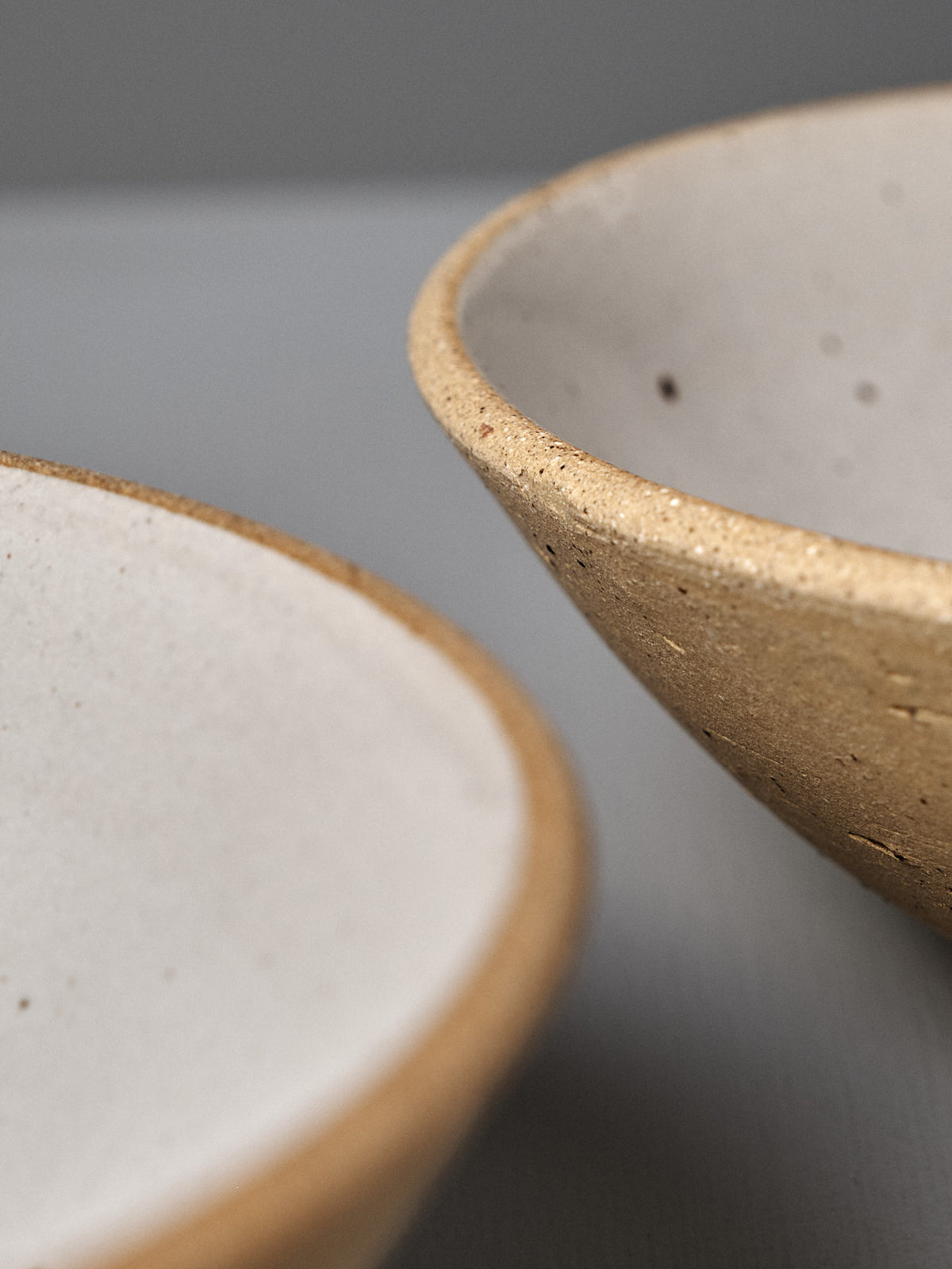 Close-up of the Speckled Toast Serving Bowl – Medium, a handmade ceramic bowl with a matte, speckled beige and white finish, displayed on a light gray surface.