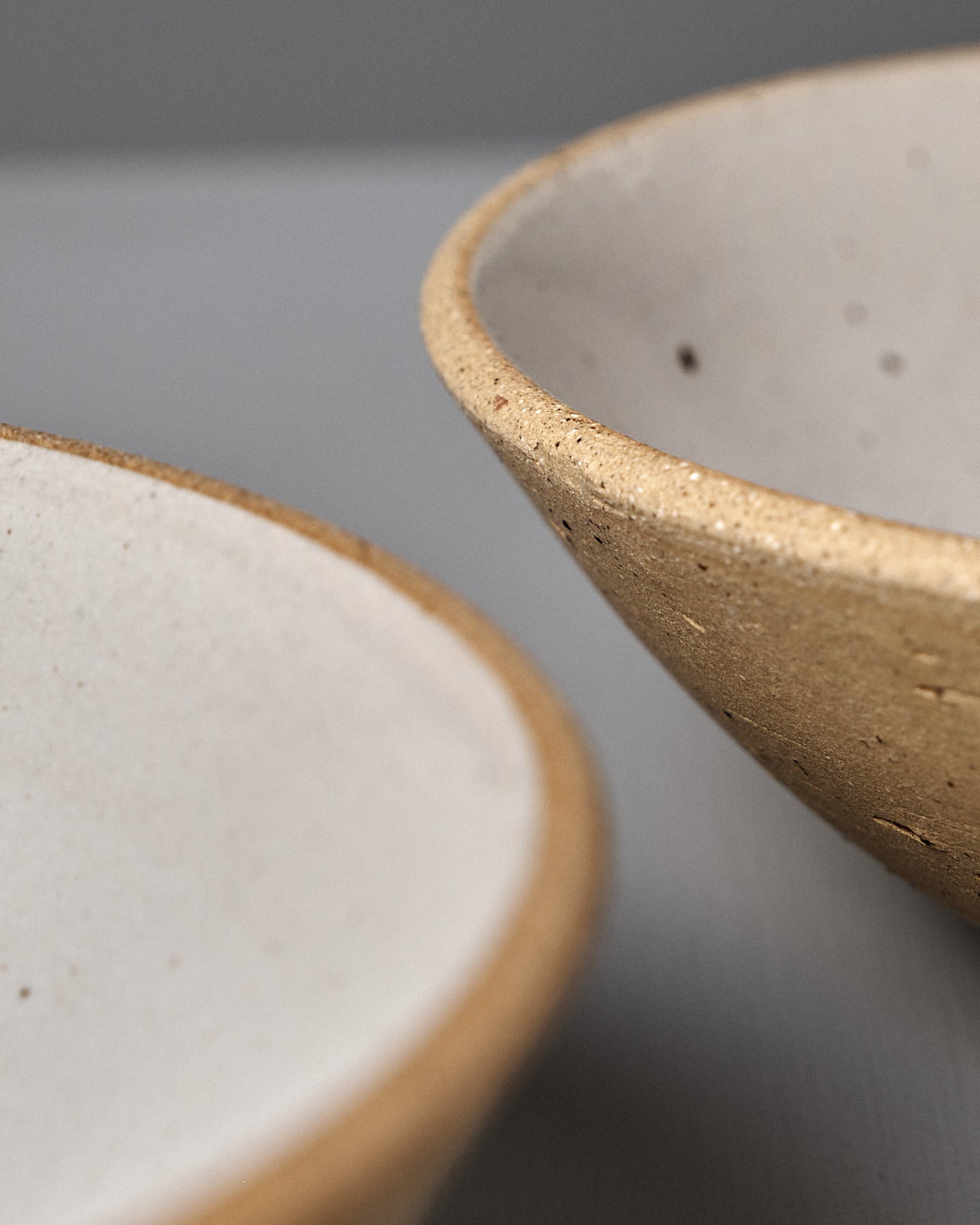 The Speckled Toast Serving Bowl – Medium is a handmade, shallow, round beige ceramic bowl with a speckled texture, displayed on a light gray surface against a plain gray background—elegantly crafted in Wellington.