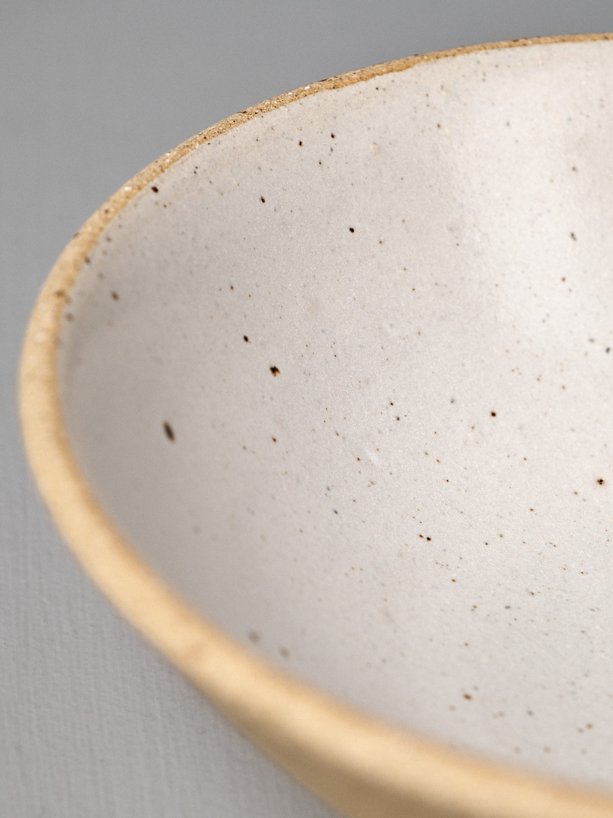 Close-up of the Speckled Toast Serving Bowl – Medium, a handmade ceramics piece featuring a speckled finish and beige rim, displayed on a neutral gray surface.