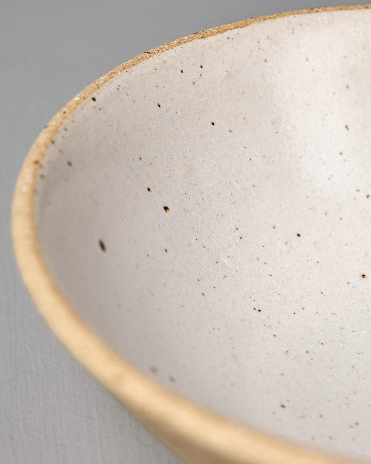 Close-up of the Speckled Toast Serving Bowl – Medium, a handmade ceramics piece featuring a speckled finish and beige rim, displayed on a neutral gray surface.