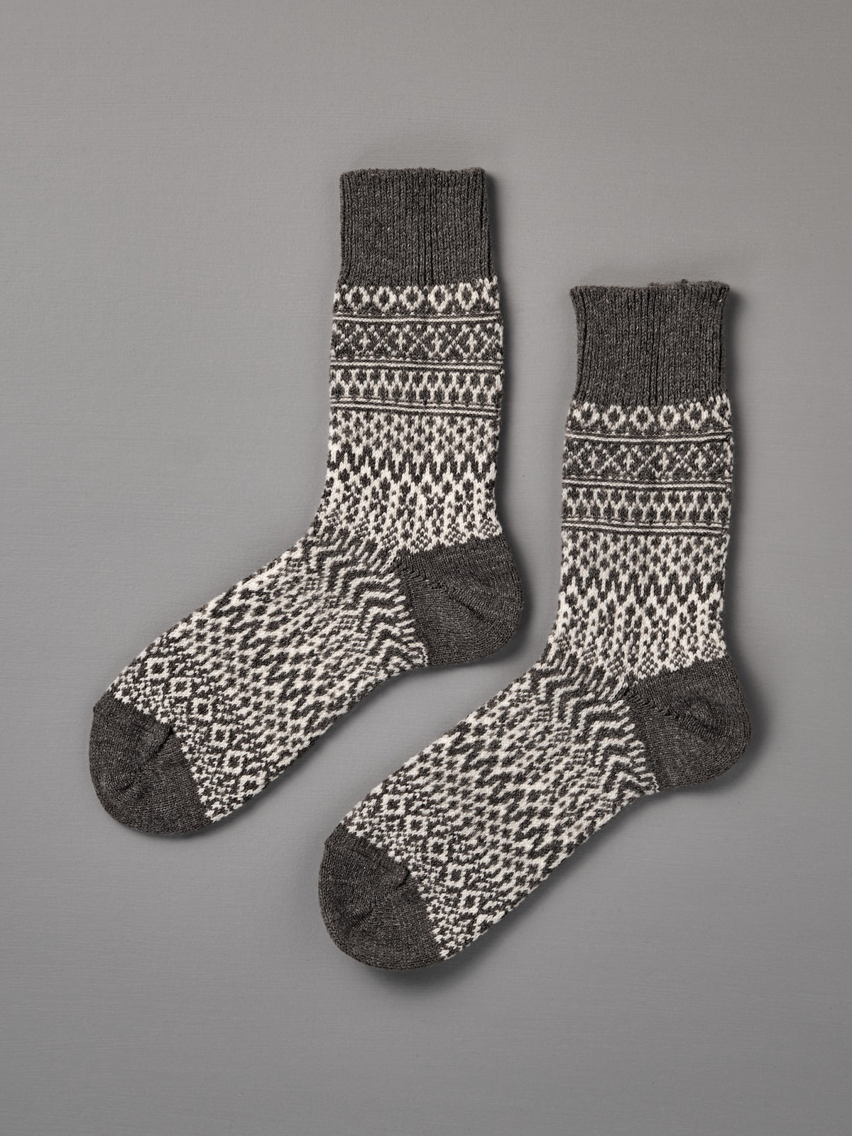 Oslo Wool Jacquard Socks – Grey: men's wool socks featuring black and white geometric patterns with dark gray heels, toes, and cuffs, displayed flat on a gray surface. Check our size chart for the perfect fit.