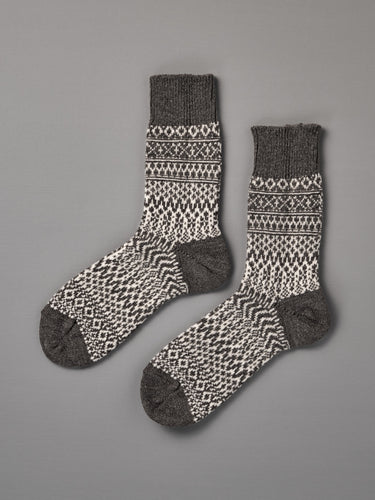 Oslo Wool Jacquard Socks – Grey: men's wool socks featuring black and white geometric patterns with dark gray heels, toes, and cuffs, displayed flat on a gray surface. Check our size chart for the perfect fit.