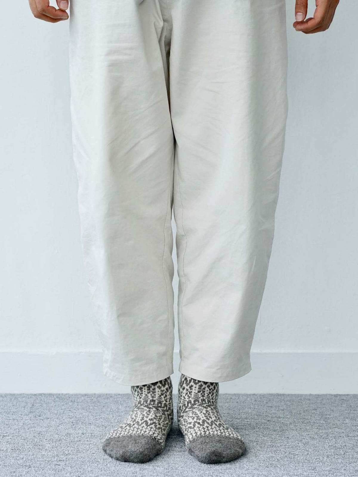 A person stands on a gray carpet wearing light pants and Oslo Wool Jacquard Socks – Grey, with their hands visible at their sides.