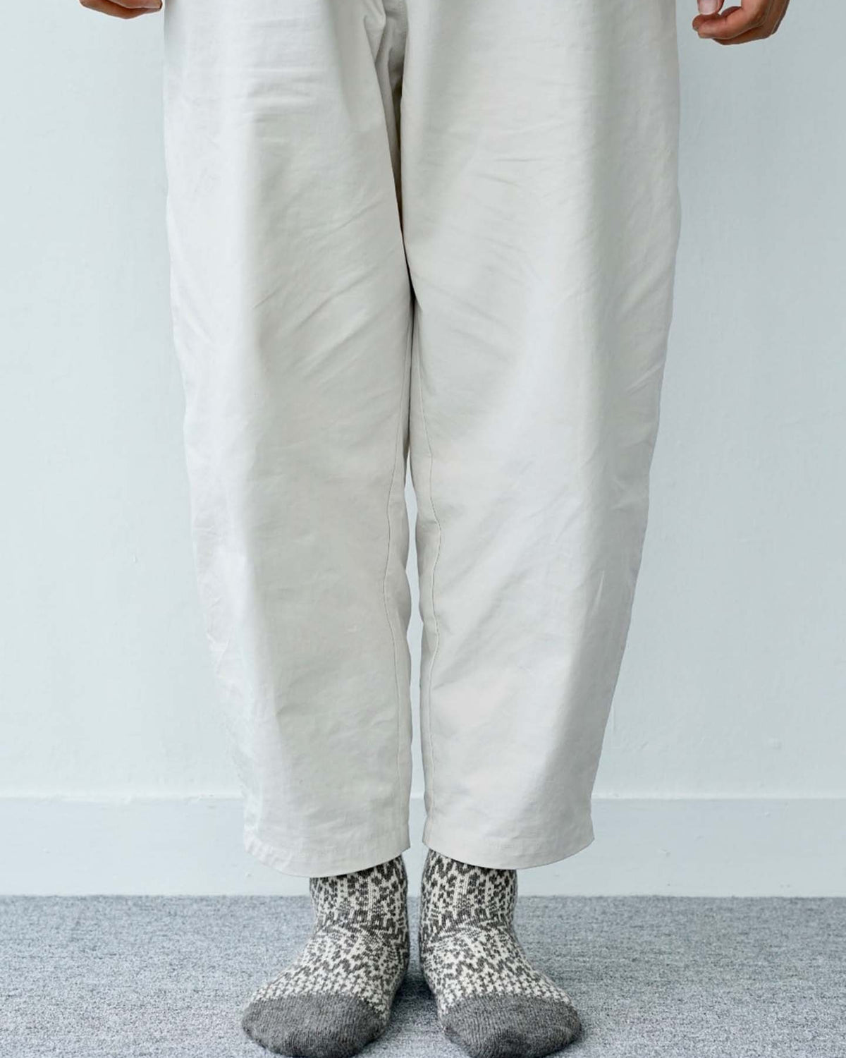 A person stands on a gray carpet wearing light pants and Oslo Wool Jacquard Socks – Grey, with their hands visible at their sides.