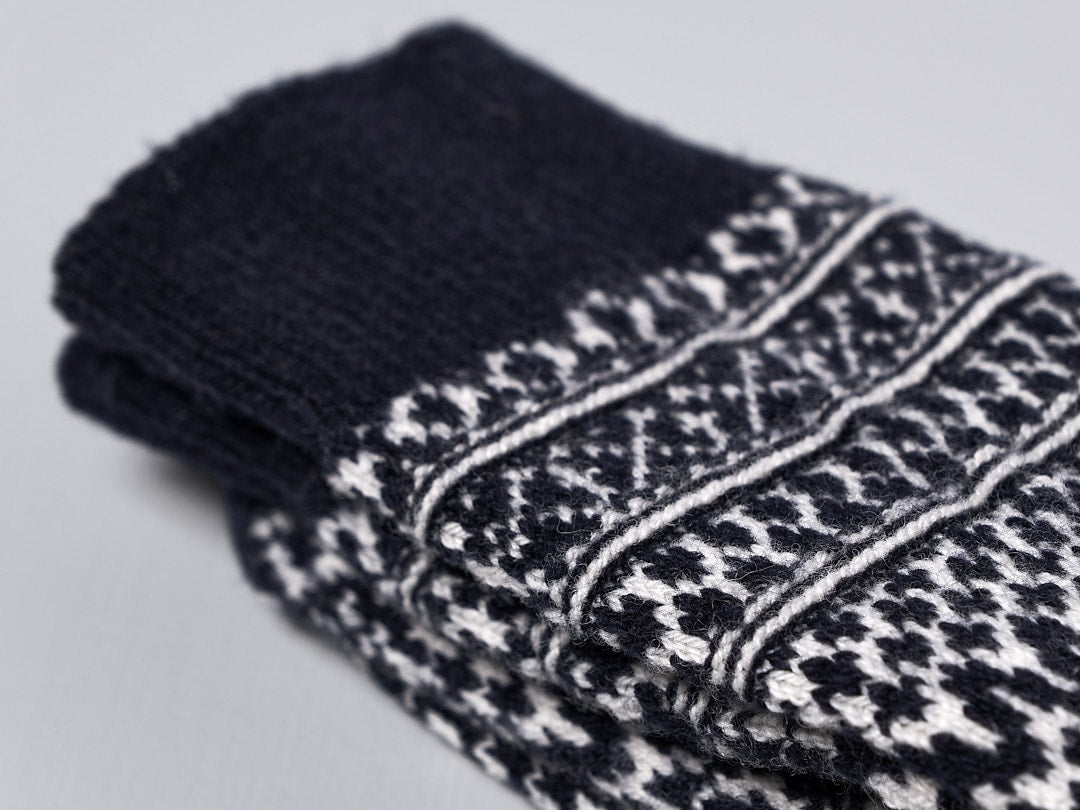A pair of Oslo Wool Jacquard Socks – Navy made by Nishiguchi Kutsushita, designed in black and white jacquard pattern knitted with pre-shrunk wool, providing incredible warmth, displayed on a white surface.