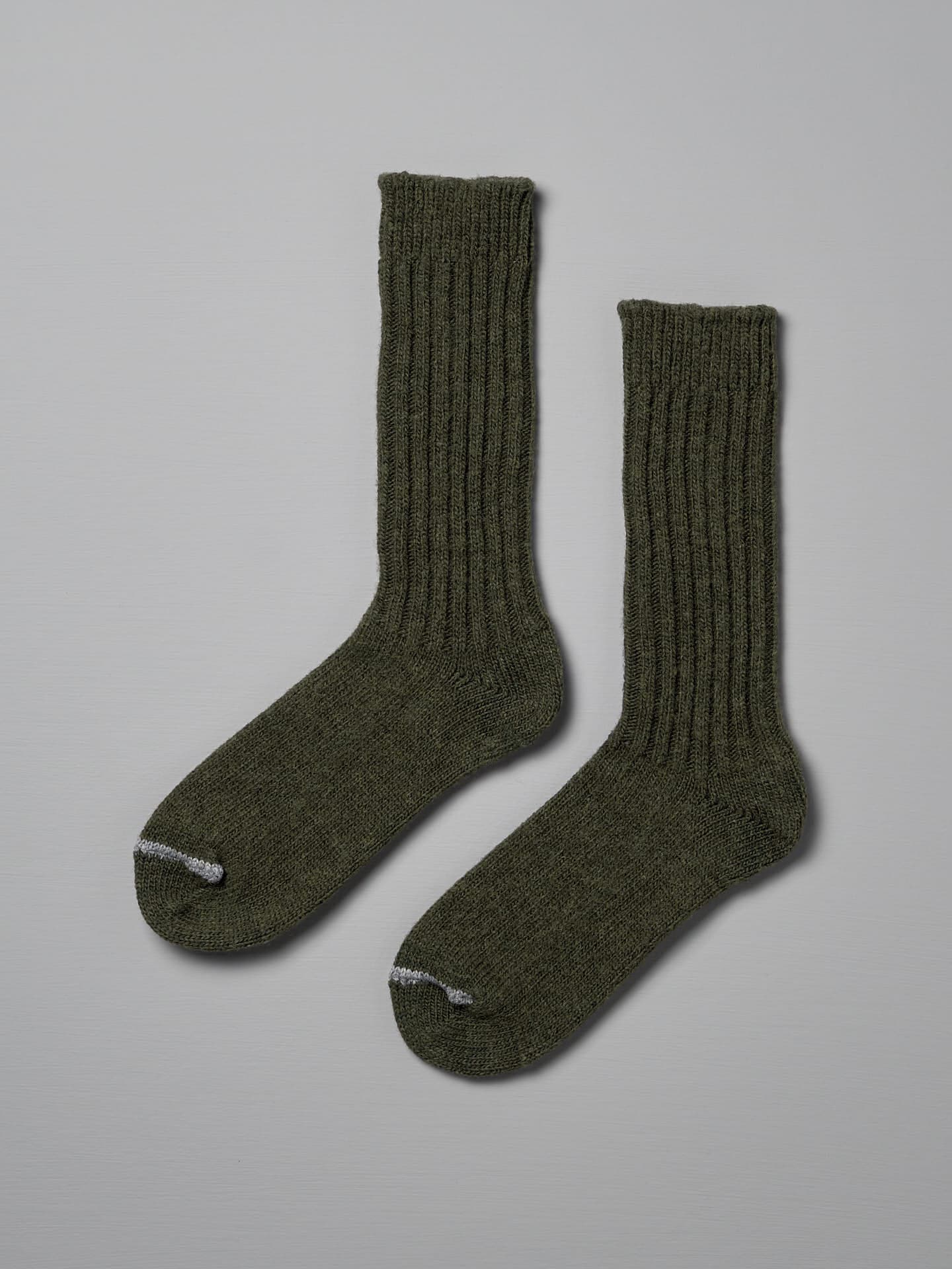 A pair of green knitted socks with ribbed cuffs and white toes, displayed side by side on a grey background, perfect for checking your Men's US size chart. Product Name: Praha Wool Ribbed Socks – Khaki Brand Name: Nishiguchi Kutsushita