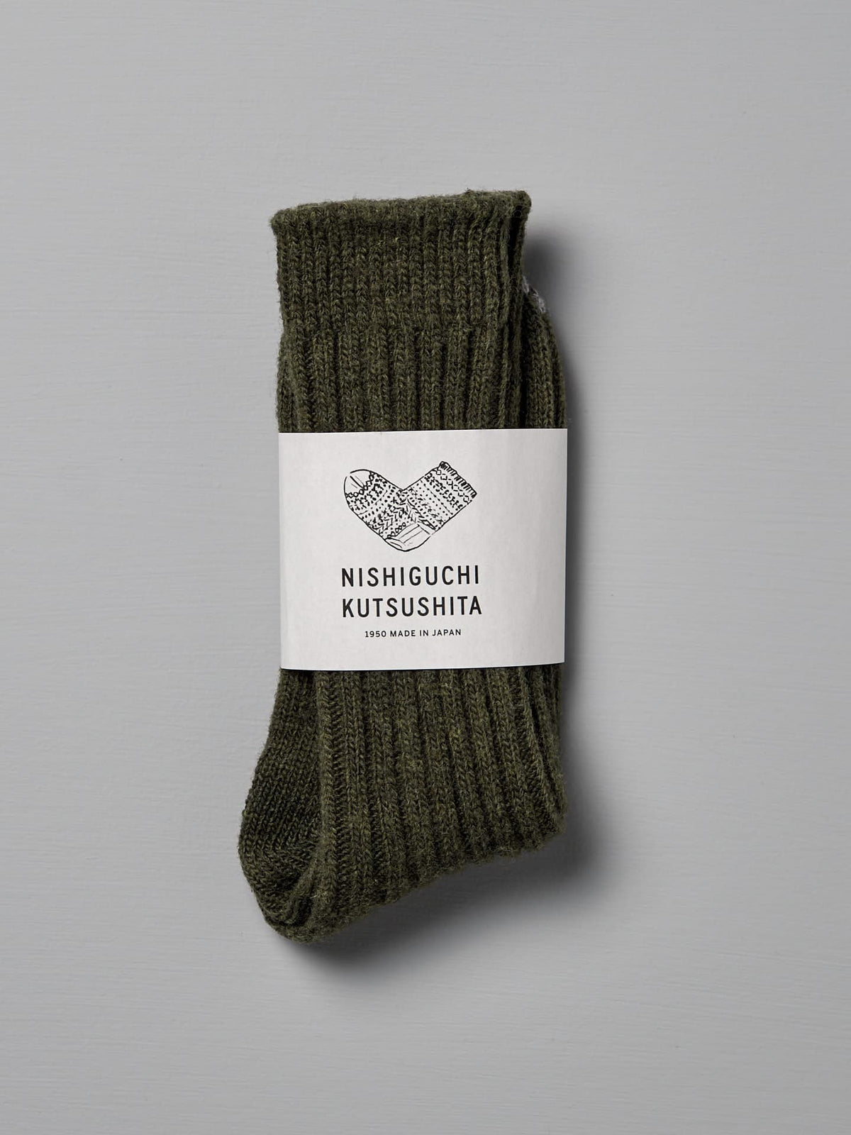 A pair of khaki wool ribbed socks folded and wrapped with a label that reads &quot;Nishiguchi Kutsushita,&quot; with text &quot;1985 Made in Japan.&quot; Includes a size chart for Men&#39;s US and Women&#39;s US.