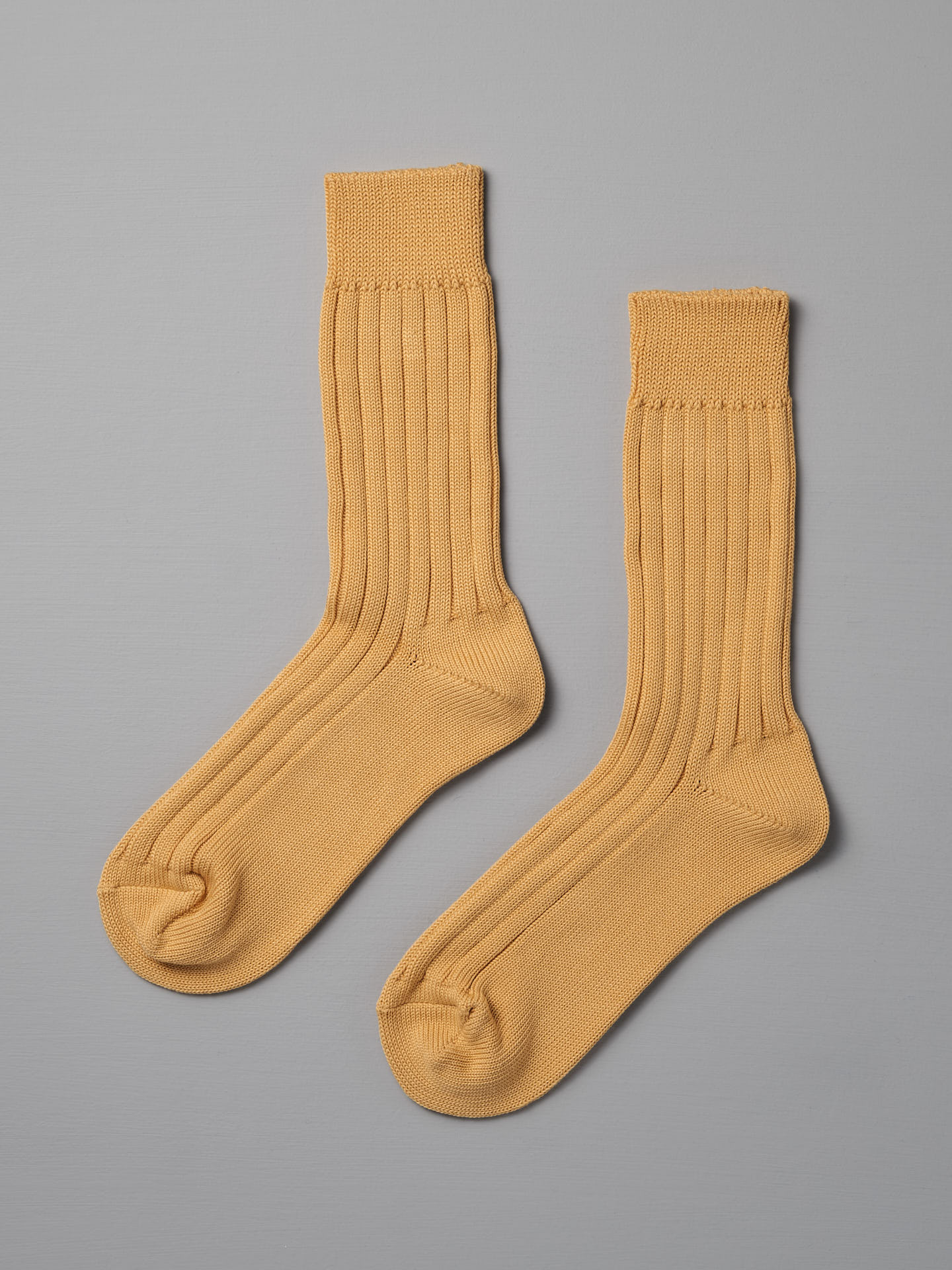 A pair of Praha Cotton Socks in Susuki-Gold by Nishiguchi Kutsushita, featuring a ribbed design for men, displayed on a flat light gray surface.