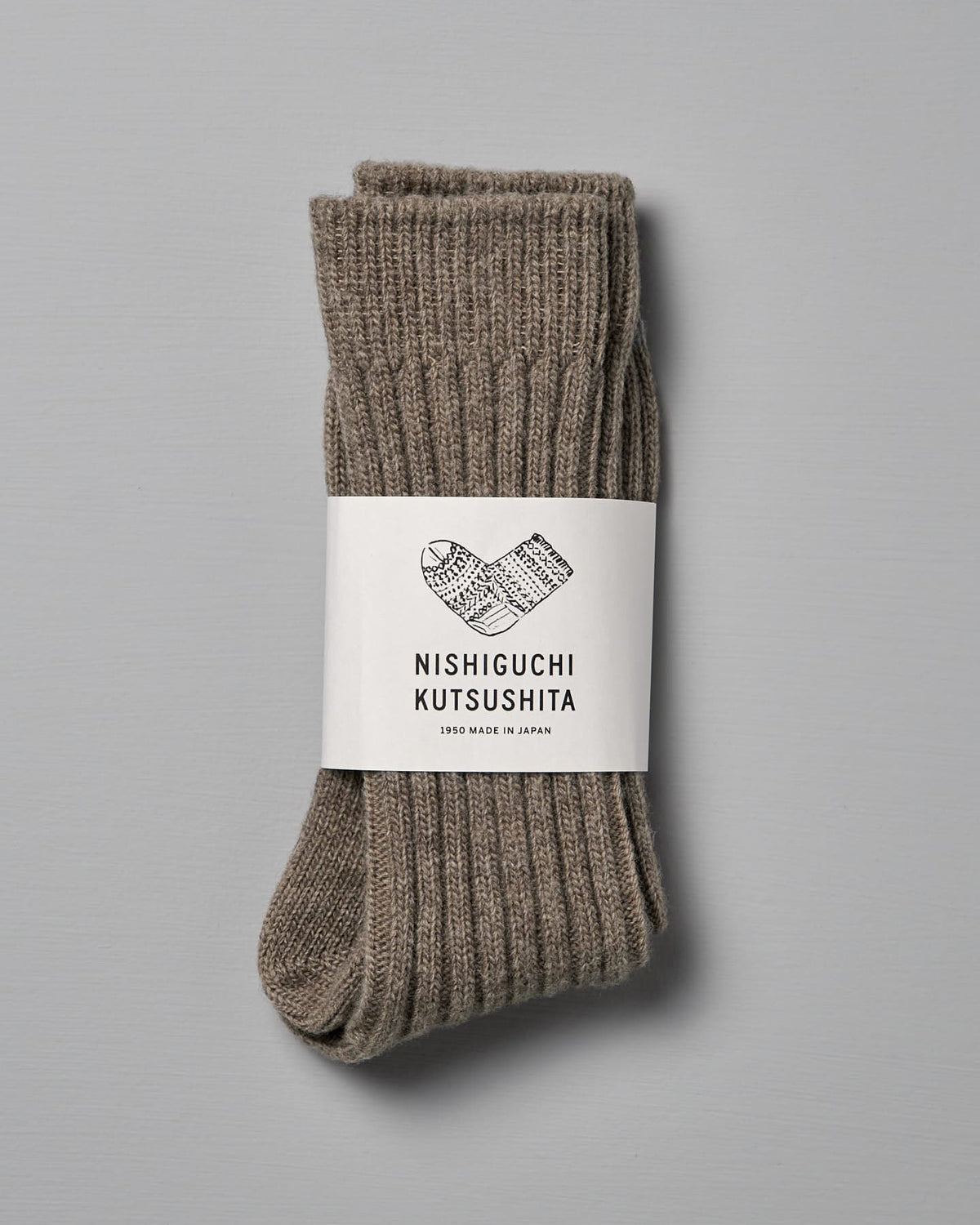 A pair of folded gray wool socks with a white label wrapped around them, highlighting the brand name "Nishiguchi Kutsushita" and "1950 Made in Japan," are available in US (Men’s) and EUR sizes.

Revised Sentence:
A pair of folded beige wool socks with a white label wrapped around them, highlighting the product name "Praha Wool Ribbed Socks – Beige" and the brand name "Nishiguchi Kutsushita," are available in US (Men’s) and EUR sizes.