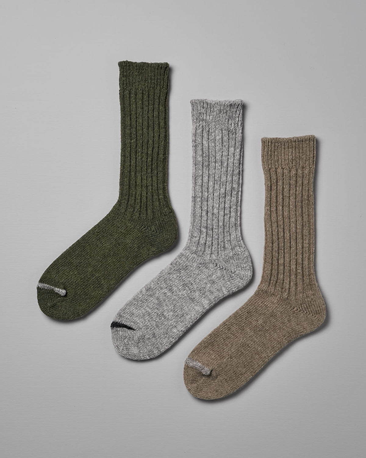 Three pairs of Praha Wool Ribbed Socks – Beige by Nishiguchi Kutsushita in green, gray, and beige colors are laid out flat against a plain gray background. Available in various sizes for both US (Women's) and EUR formats.