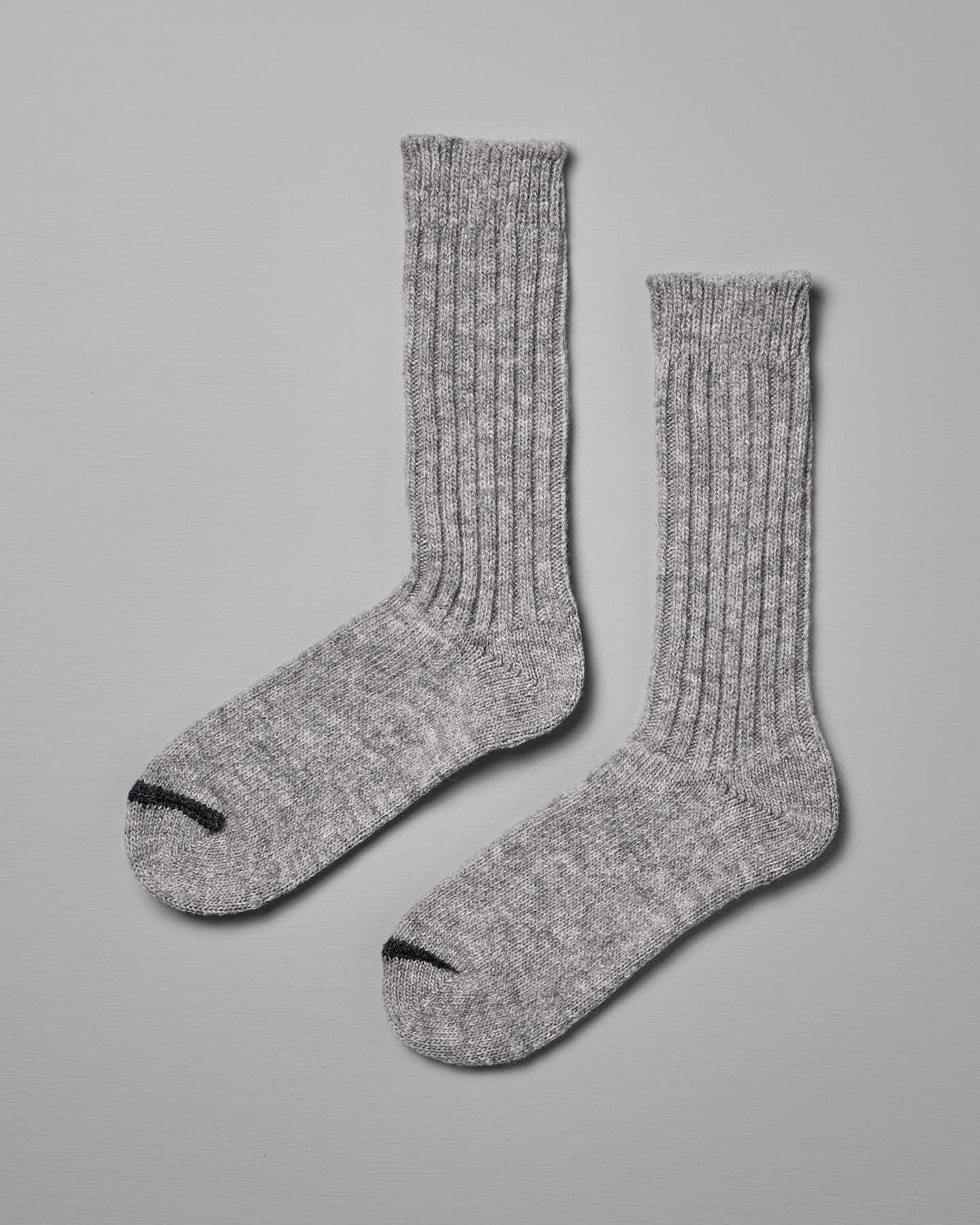 A pair of Praha Wool Ribbed Socks – Light Grey by Nishiguchi Kutsushita with ribbed texture and black toe tips, displayed against a light gray background, ideal for pairing with women's shoes.