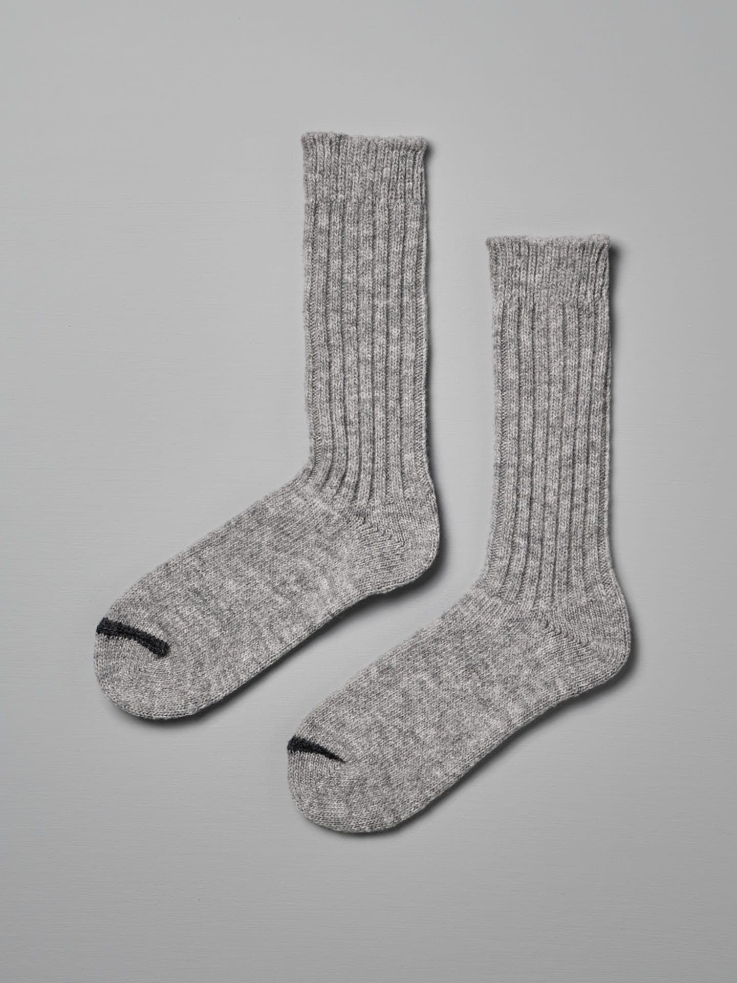 A pair of Praha Wool Ribbed Socks – Light Grey by Nishiguchi Kutsushita with ribbed texture and black toe tips, displayed against a light gray background, ideal for pairing with women's shoes.