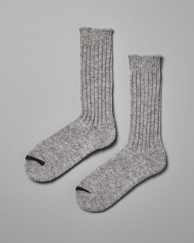 A pair of Praha Wool Ribbed Socks – Light Grey by Nishiguchi Kutsushita with ribbed texture and black toe tips, displayed against a light gray background, ideal for pairing with women's shoes.