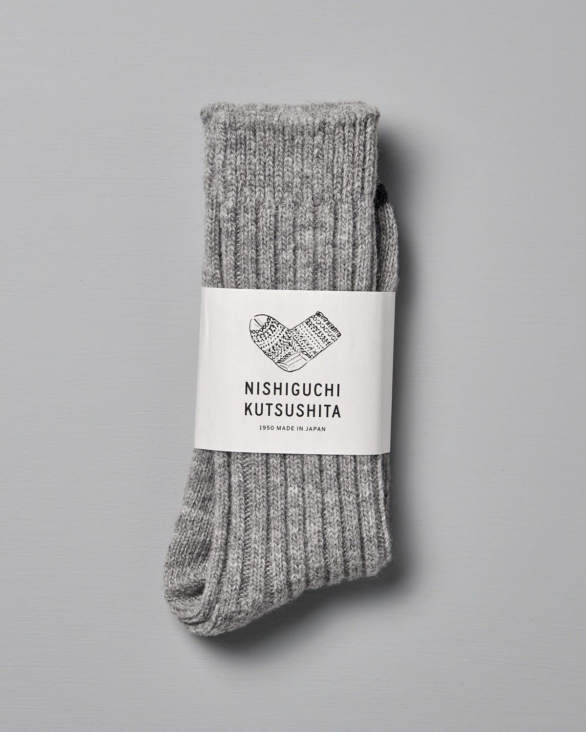 A pair of gray, ribbed Nishiguchi Kutsushita Praha Wool Ribbed Socks – Light Grey with a white label displaying the brand name, "Made in Japan" text, and US Men's sizes against a plain background.