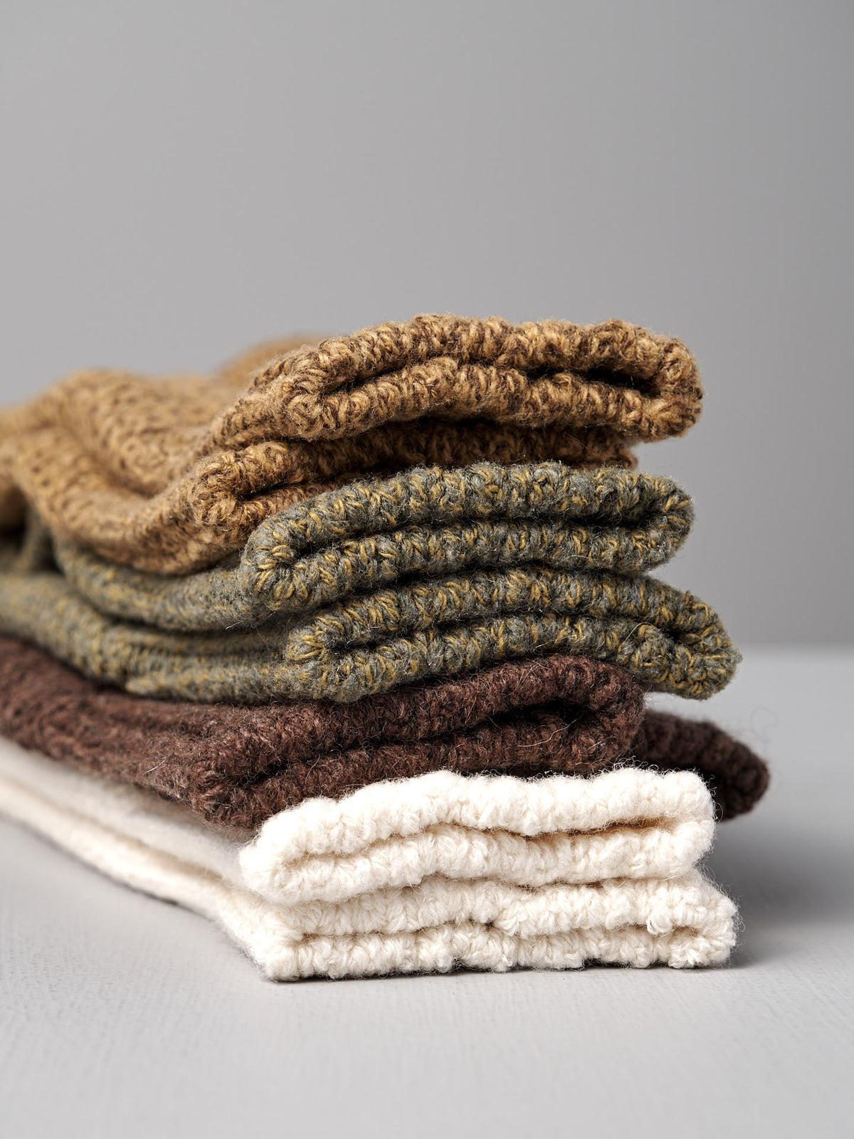 Four folded Wool Cotton Boot Socks in brown by Nishiguchi Kutsushita are stacked on a light gray surface—versatile accessories to elevate any look, just like finding the perfect women&#39;s fit.