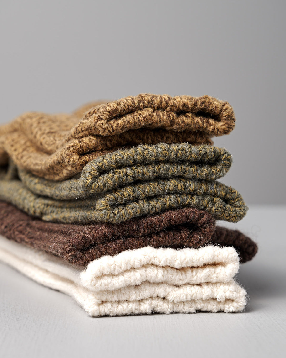 Four folded Wool Cotton Boot Socks in brown by Nishiguchi Kutsushita are stacked on a light gray surface—versatile accessories to elevate any look, just like finding the perfect women's fit.