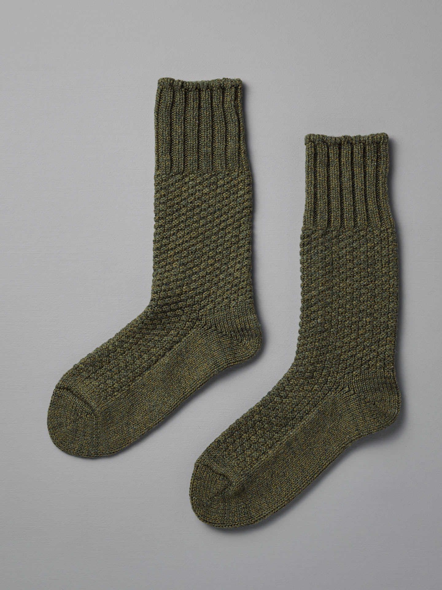 A pair of Nishiguchi Kutsushita Wool Cotton Boot Socks in moss green, shown textured and laid flat on a light gray surface, suitable for US and EUR men’s shoe sizes.
