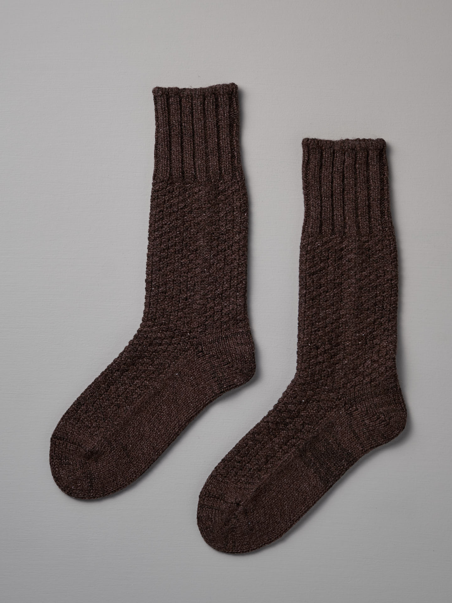 A pair of dark brown, knitted wool socks with a ribbed cuff placed side by side on a light gray background, available in both US Men's sizes and EUR sizes, **Wool Cotton Boot Socks – Brown** by **Nishiguchi Kutsushita**.
