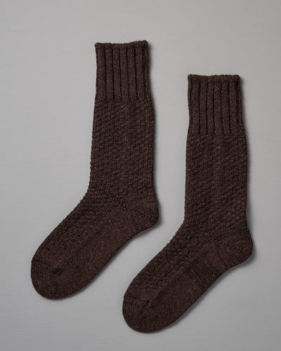 A pair of dark brown, knitted wool socks with a ribbed cuff placed side by side on a light gray background, available in both US Men's sizes and EUR sizes, **Wool Cotton Boot Socks – Brown** by **Nishiguchi Kutsushita**.
