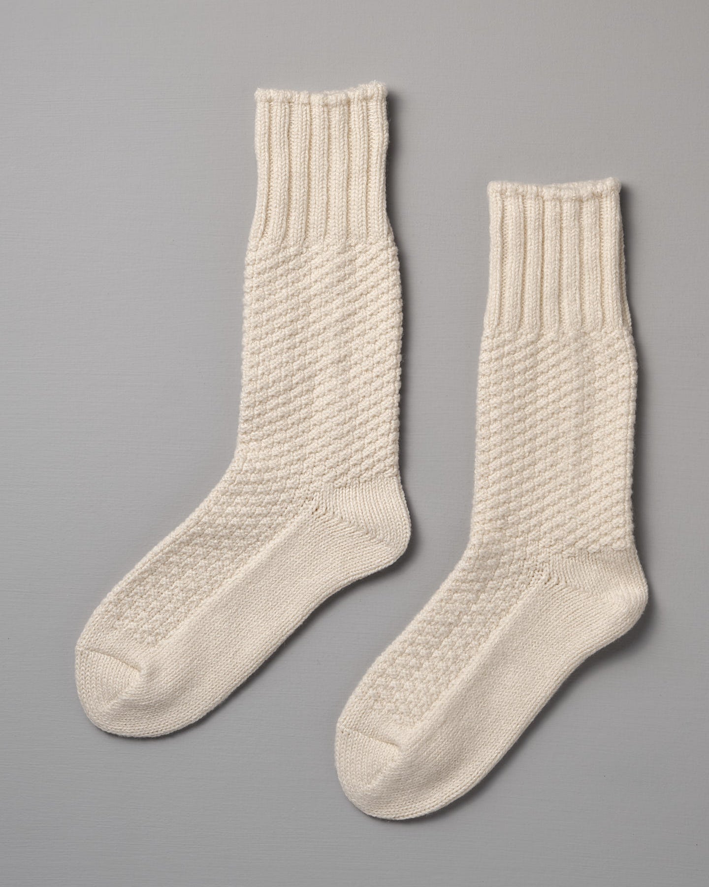 A pair of Nishiguchi Kutsushita Wool Cotton Boot Socks – Ivory with ribbed cuffs and a textured pattern on a gray background, available in Men's US and Women's US sizes.